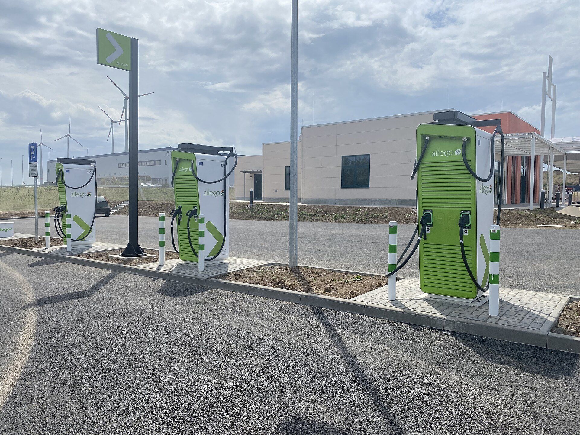 Three green-and-white Allego DC fast-charging units with hanging cables at an Autohof motorway service area in Wörrstadt, Germany