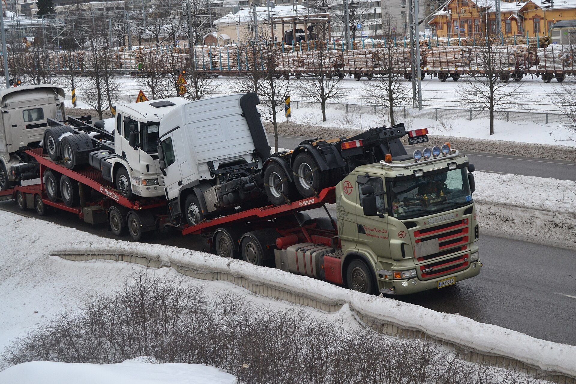 A Scania R500 vehicle transporter with a drawbar trailer carrying new white trucks without bodies on a snowy road in Jyväskylä, Finland