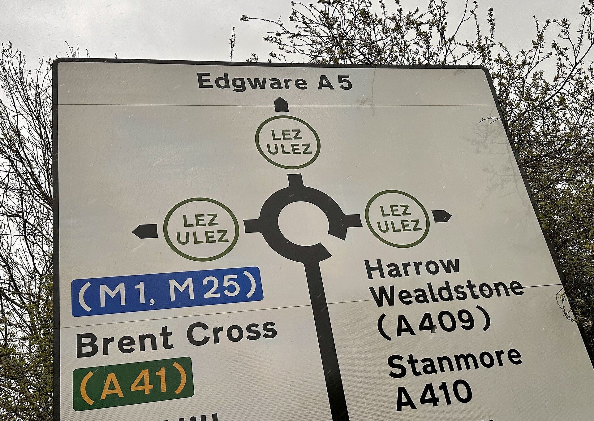 Roundabout direction sign in Harrow, north-west London, with a green LEZ and ULEZ roundel on each exit, towards Edgware (A5), Brent Cross (A41) for the M1 and M25, and Harrow, Wealdstone and Stanmore