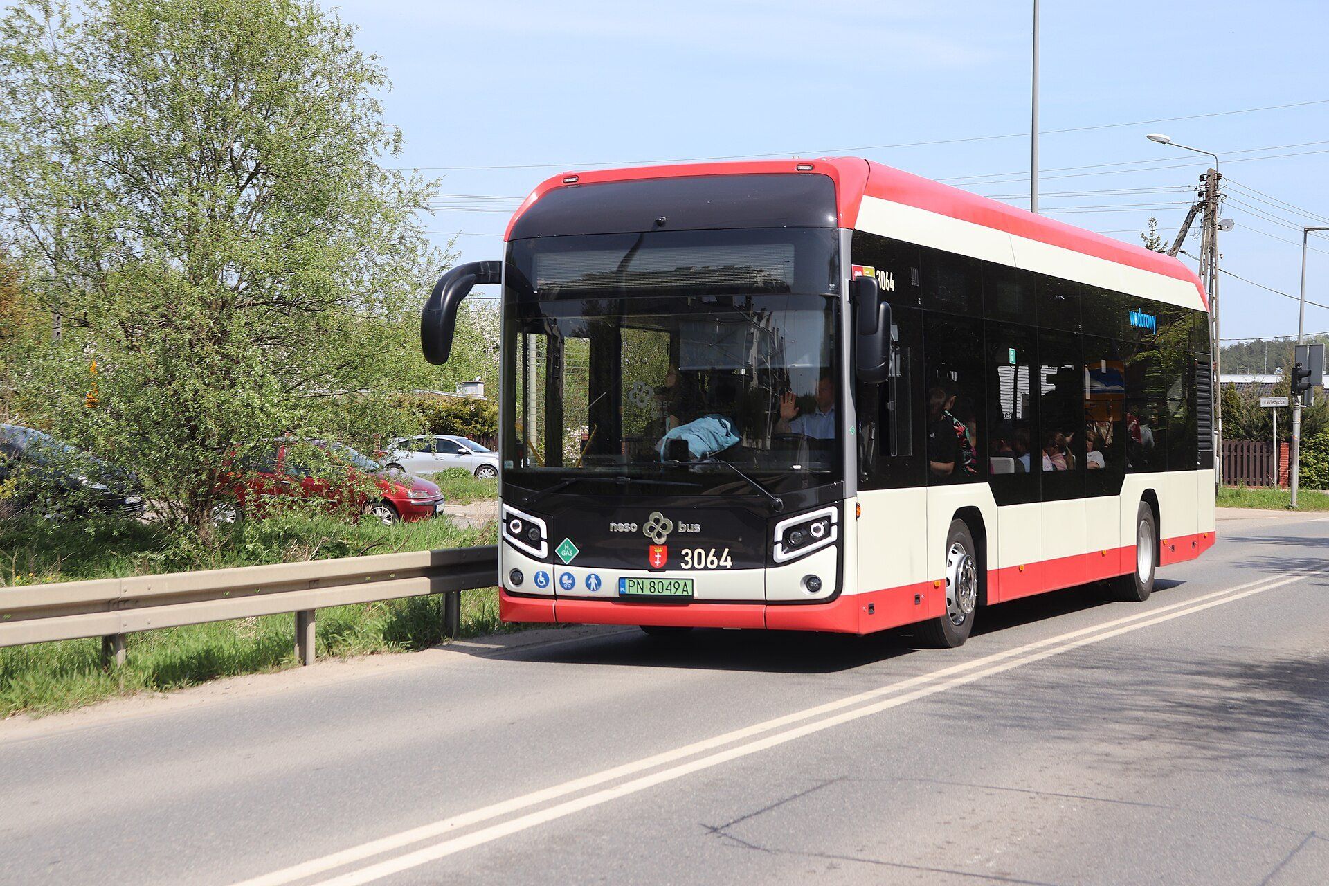 Red and cream city bus with the Gdańsk coat of arms on its front, marked 'wodorowy' (Polish for hydrogen) on the side, driving along a sunny road in Gdańsk
