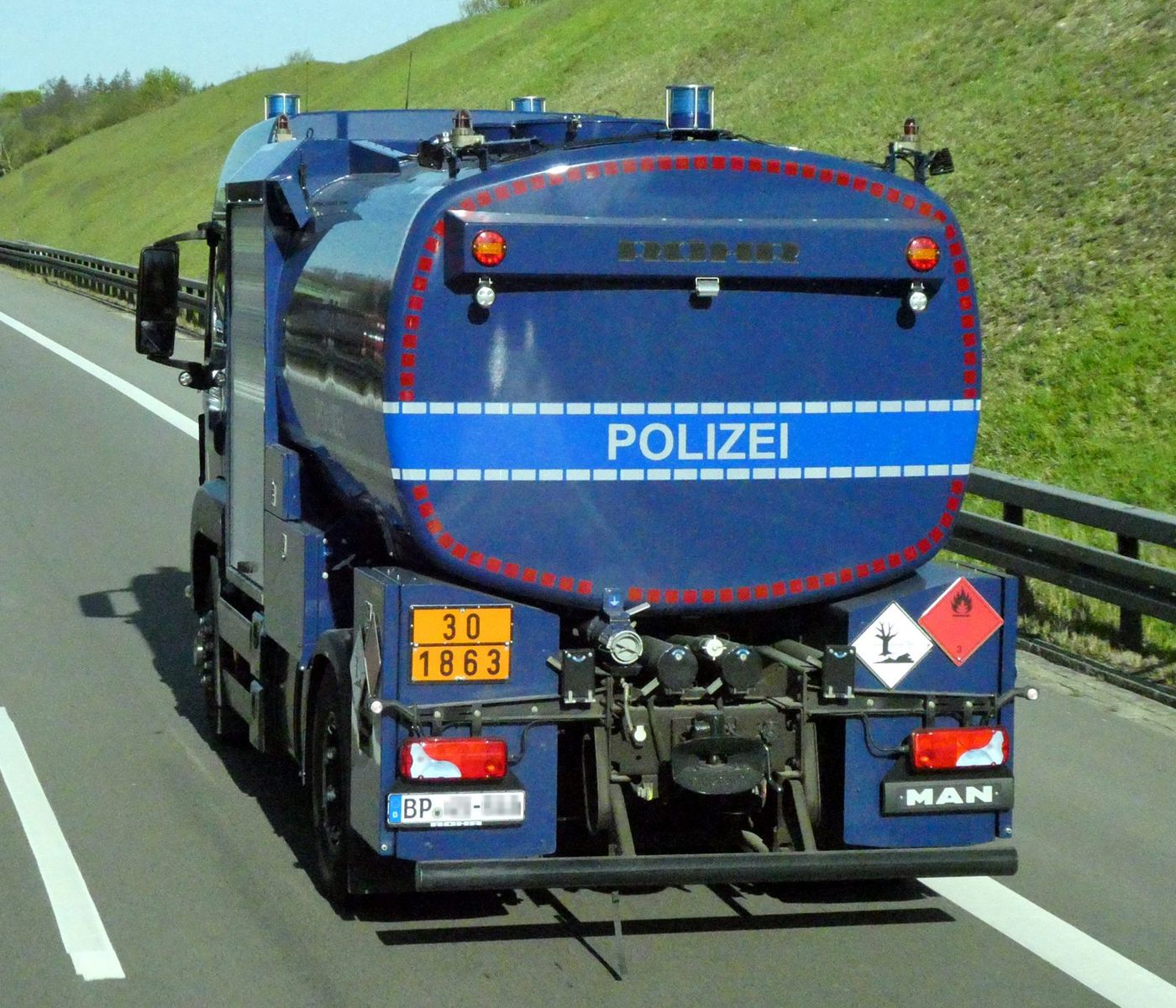 Blauer Tankwagen der Bundespolizei von hinten auf einer mehrspurigen Straße, mit orangefarbener Warntafel 30 über 1863, Gefahrzettel der Klasse 3 und dem Kennzeichen für umweltgefährdende Stoffe