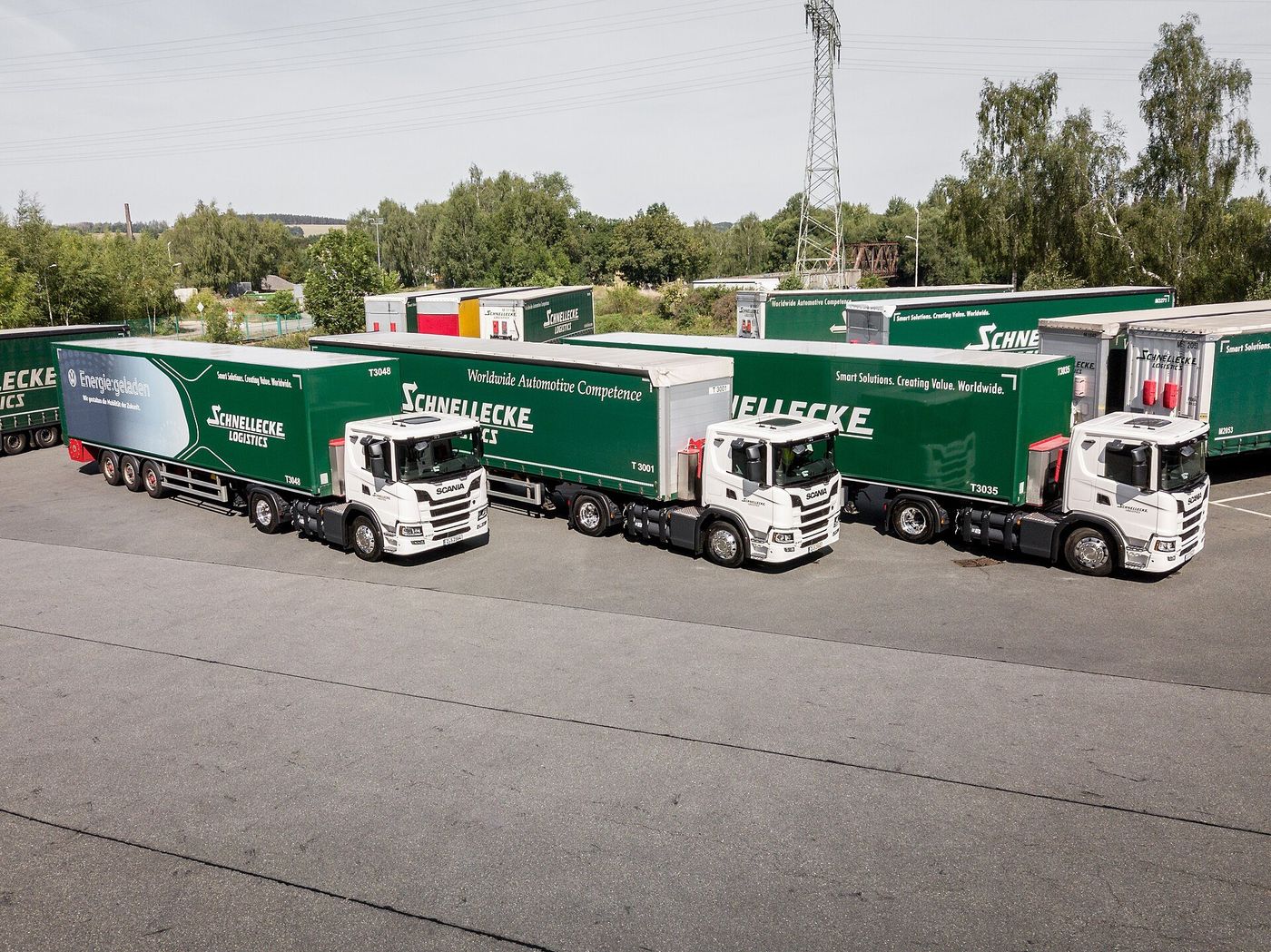 Drei Sattelzüge mit weißen Scania-Zugmaschinen und grünen Aufliegern von Schnellecke Logistics auf einem Betriebsgelände in Zwickau