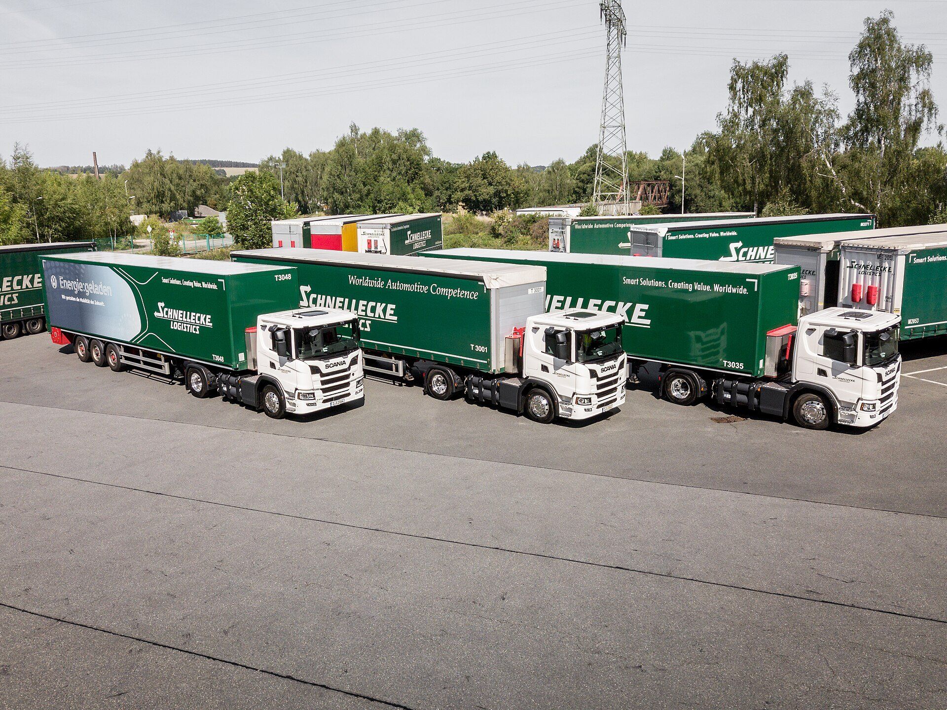 Drei Sattelzüge mit weißen Scania-Zugmaschinen und grünen Aufliegern von Schnellecke Logistics auf einem Betriebsgelände in Zwickau