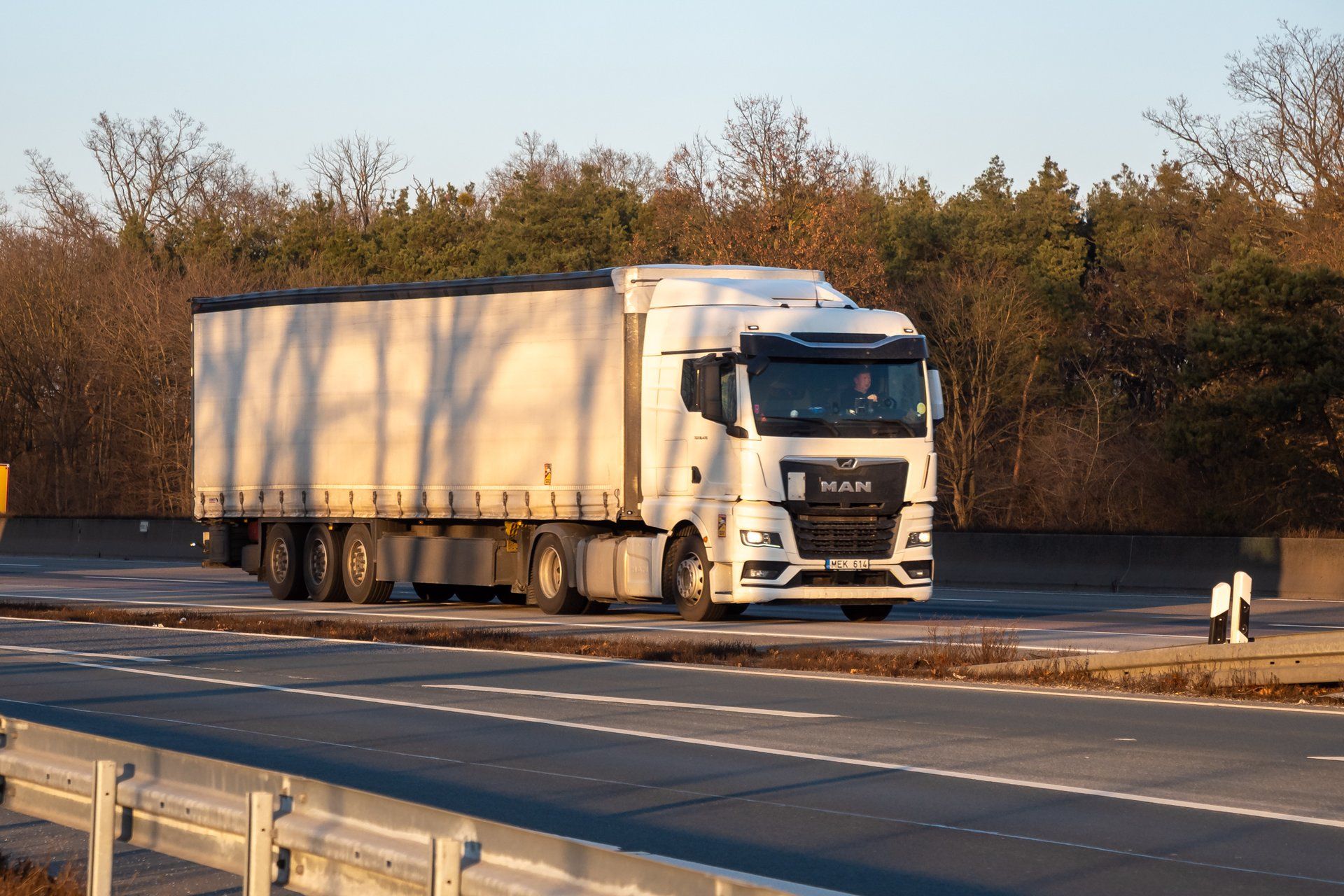 Weißer Sattelzug mit MAN-Zugmaschine und dreiachsigem Planenauflieger auf der Bundesautobahn 5 in der Nähe des Frankfurter Flughafens