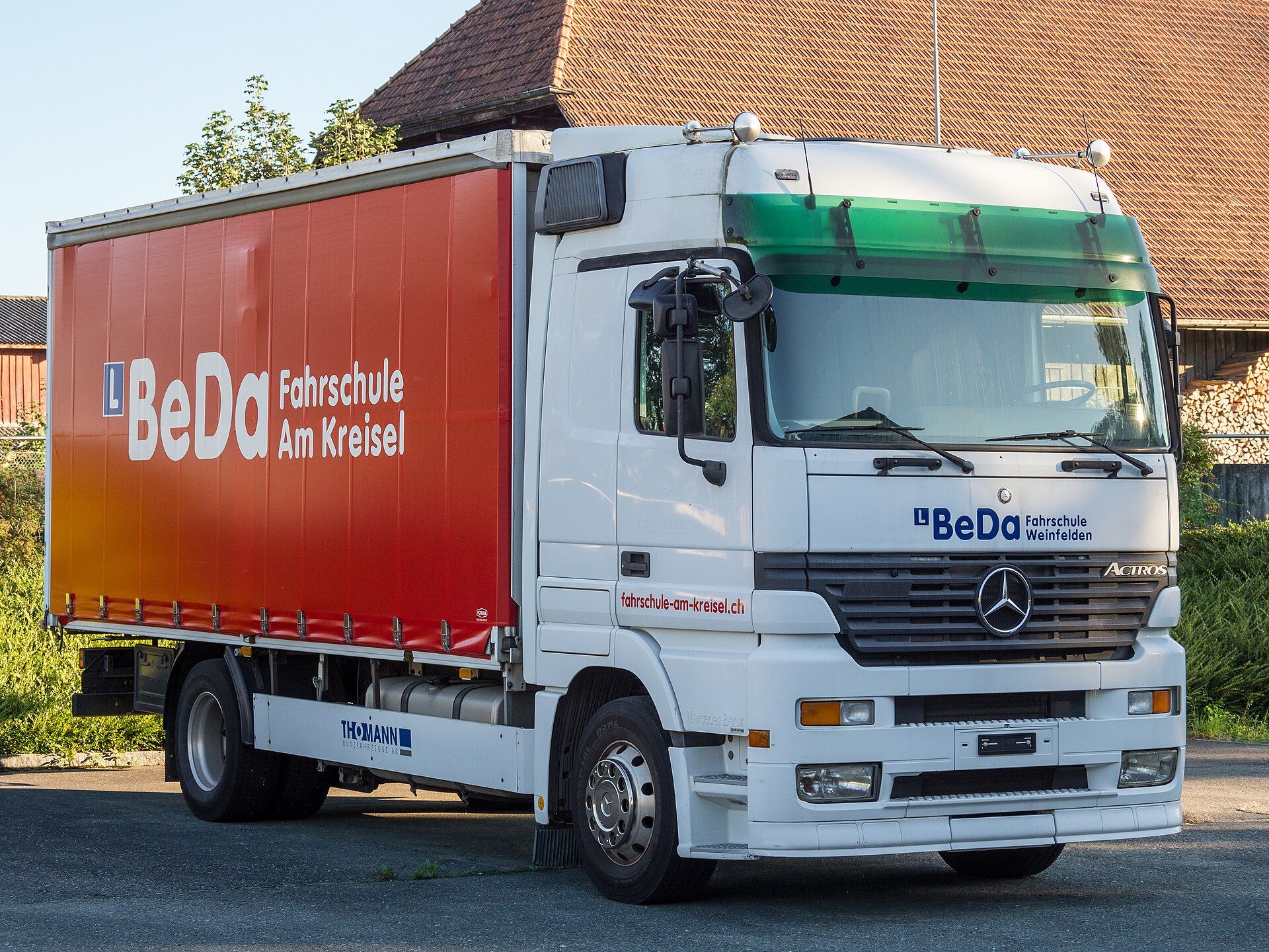 Mercedes-Benz Actros Solo-Lkw mit Curtainsider-Aufbau in Fahrschul-Lackierung, mit L-Schild, geparkt in Bürglen in der Schweiz
