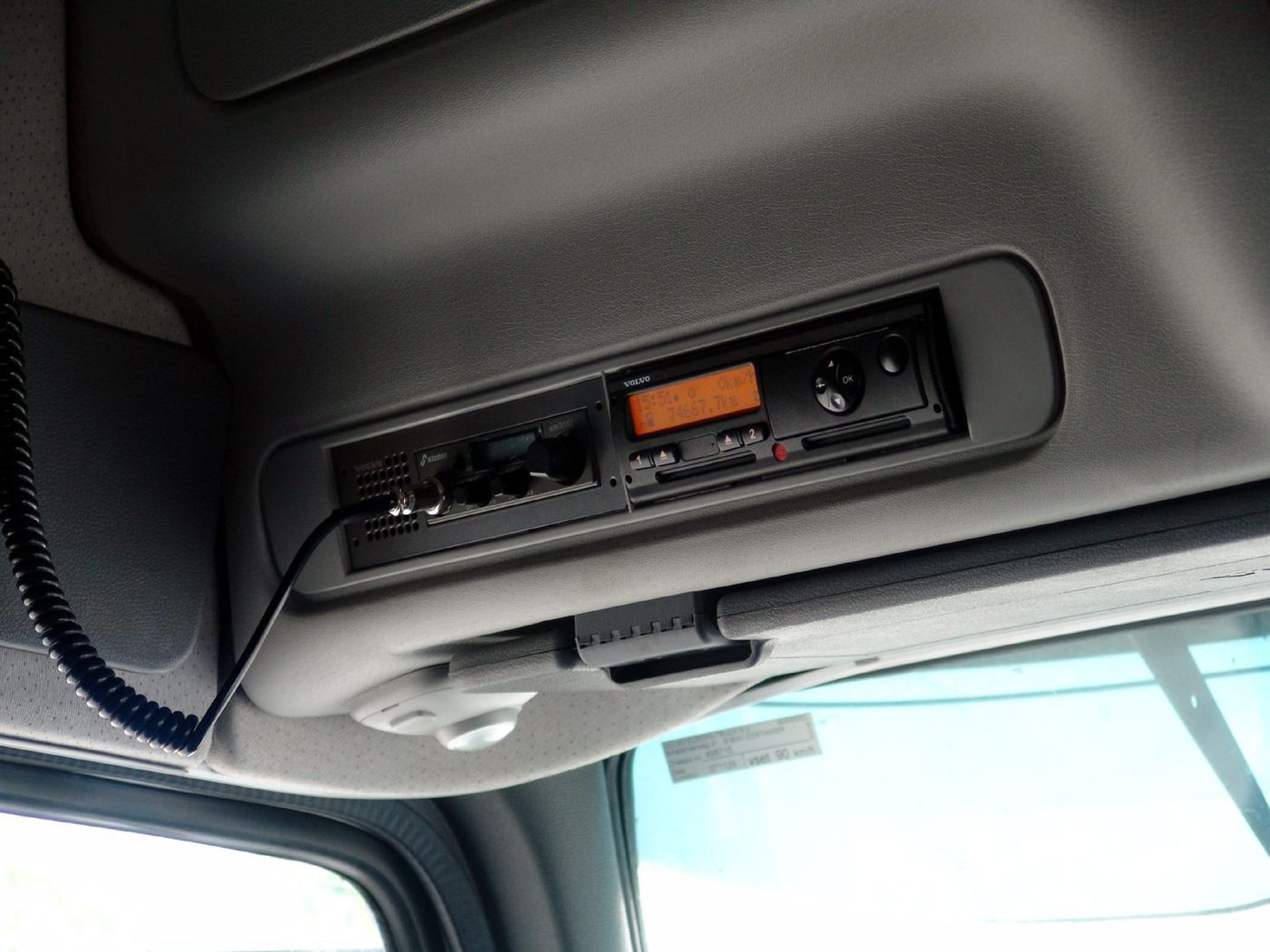 Tachigrafo digitale con il marchio Volvo e due fessure per le carte del conducente nella consolle superiore della cabina di un camion, accanto a una radio CB