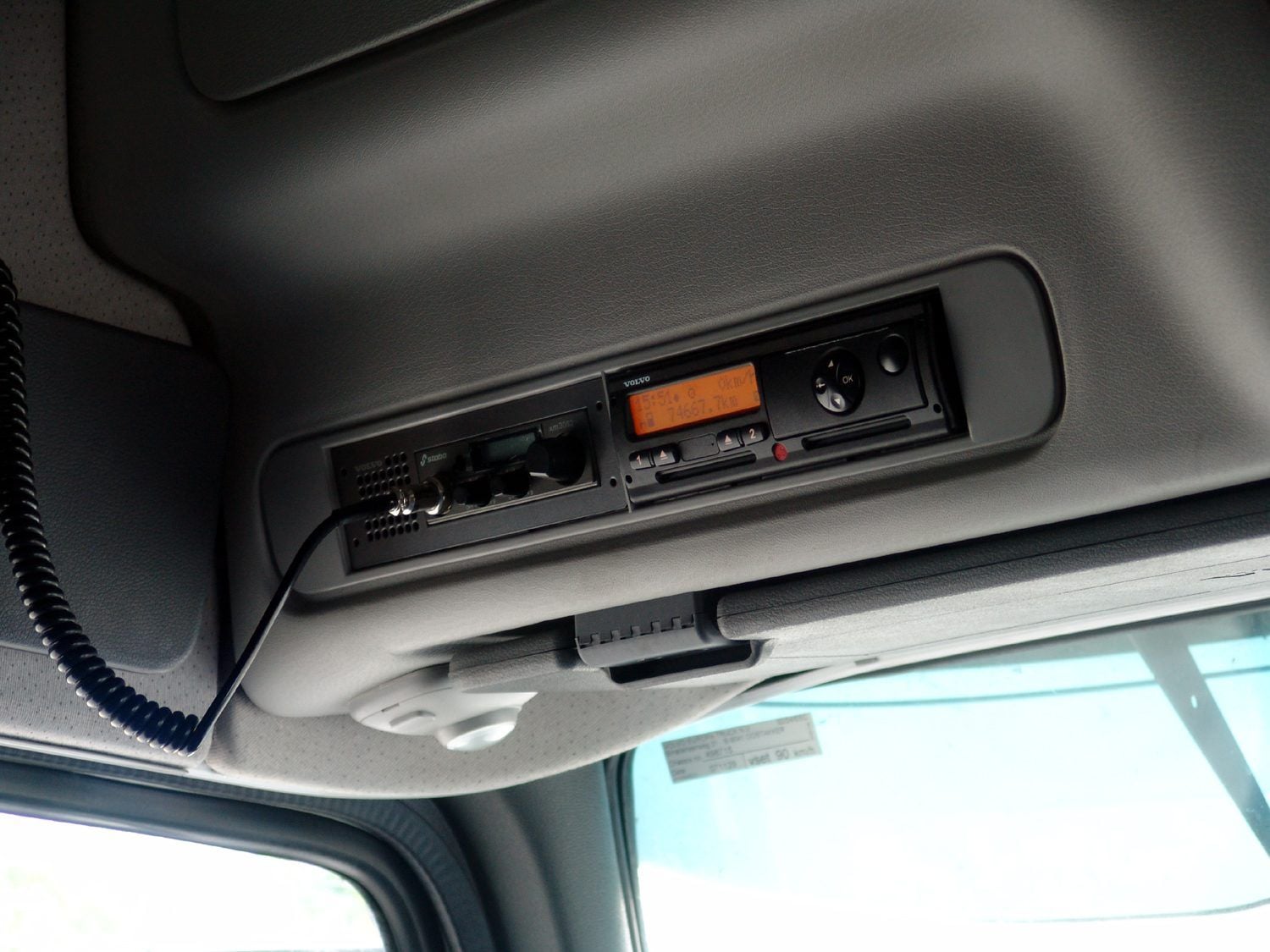 Volvo-branded digital tachograph with two driver card slots in the overhead console of a truck cab, beside a CB radio