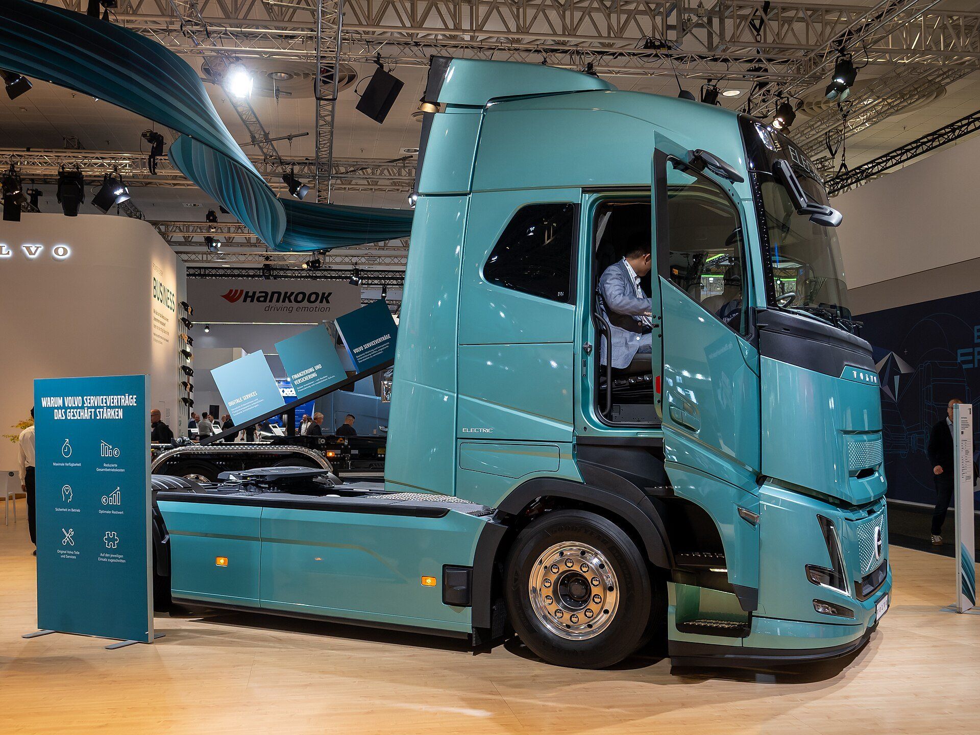 Teal Volvo FH Electric tractor unit with the cab door open on a trade-fair stand, ELECTRIC lettering on the cab side