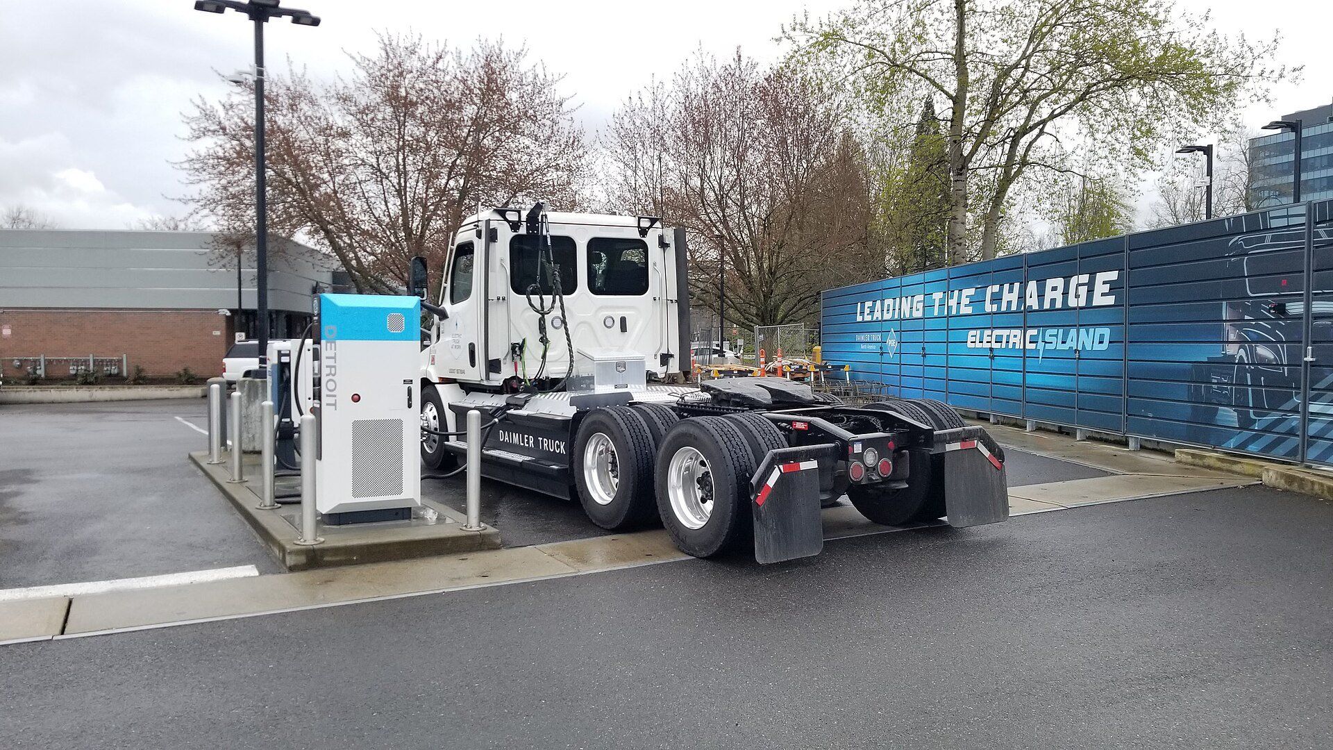 Un trattore stradale Freightliner eCascadia bianco parcheggiato accanto a una colonnina di ricarica in corrente continua con i cavi di ricarica collegati