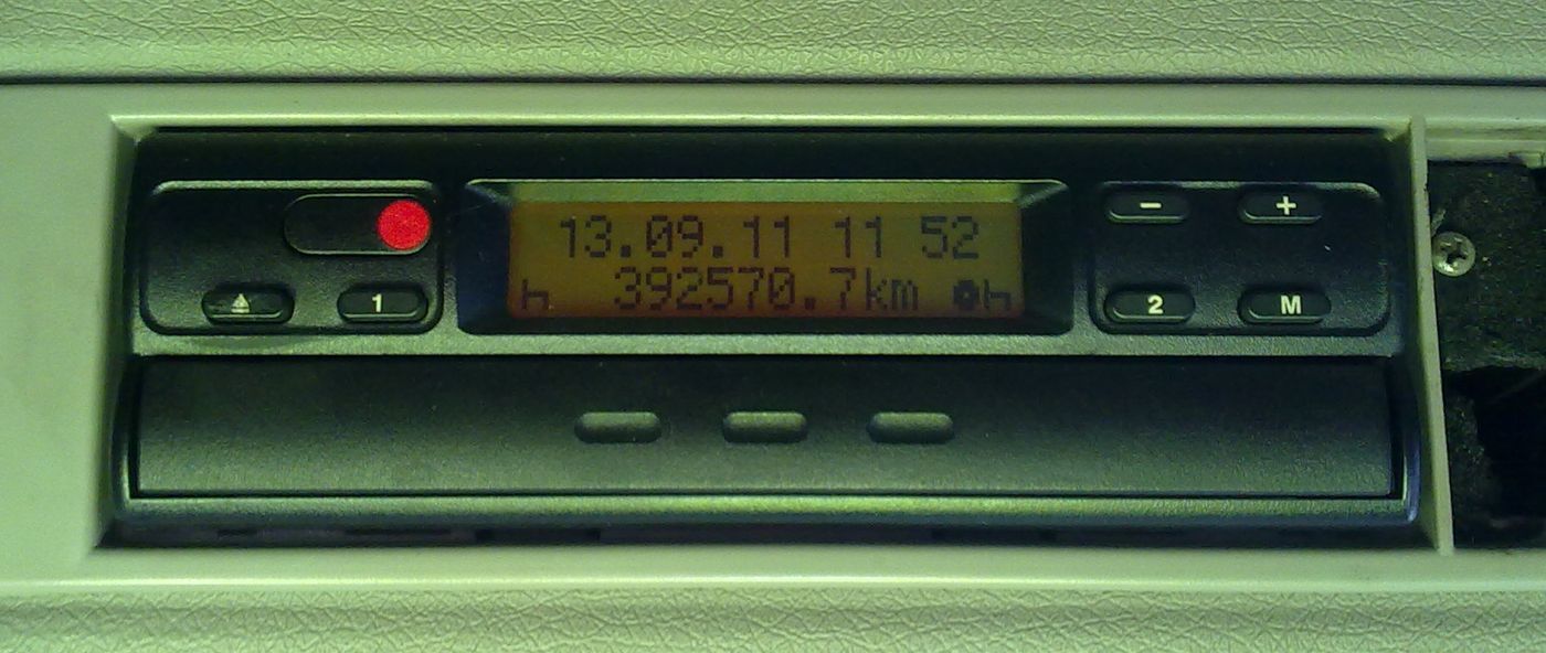 Tacógrafo Siemens VDO MTCO 1324 encastrado en un panel gris de la cabina, con la pantalla iluminada que muestra 13.09.11, 11 52 y 392570.7 km junto a los botones 1, 2, M, + y −