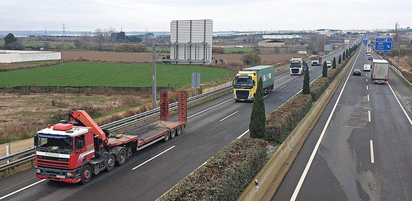 Camiones circulando por una autovía española en ambos sentidos, con un panel de salida hacia Tudela y Fitero al fondo