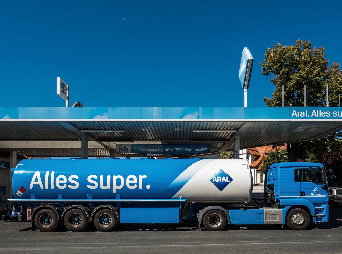 Blue road fuel tanker semi-trailer parked in front of a petrol station canopy in Bamberg, Germany