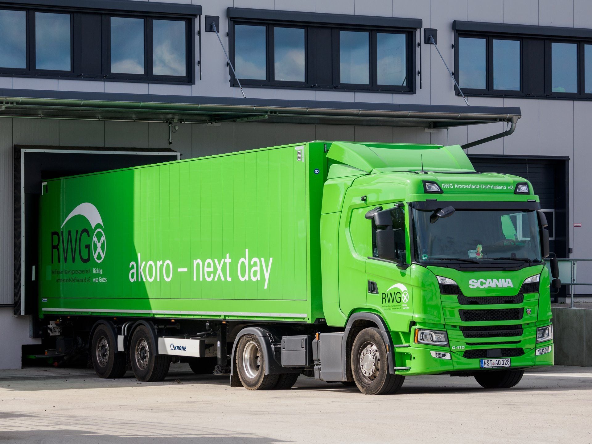 A green Scania G 410 tractor unit with a box semi-trailer at a loading dock