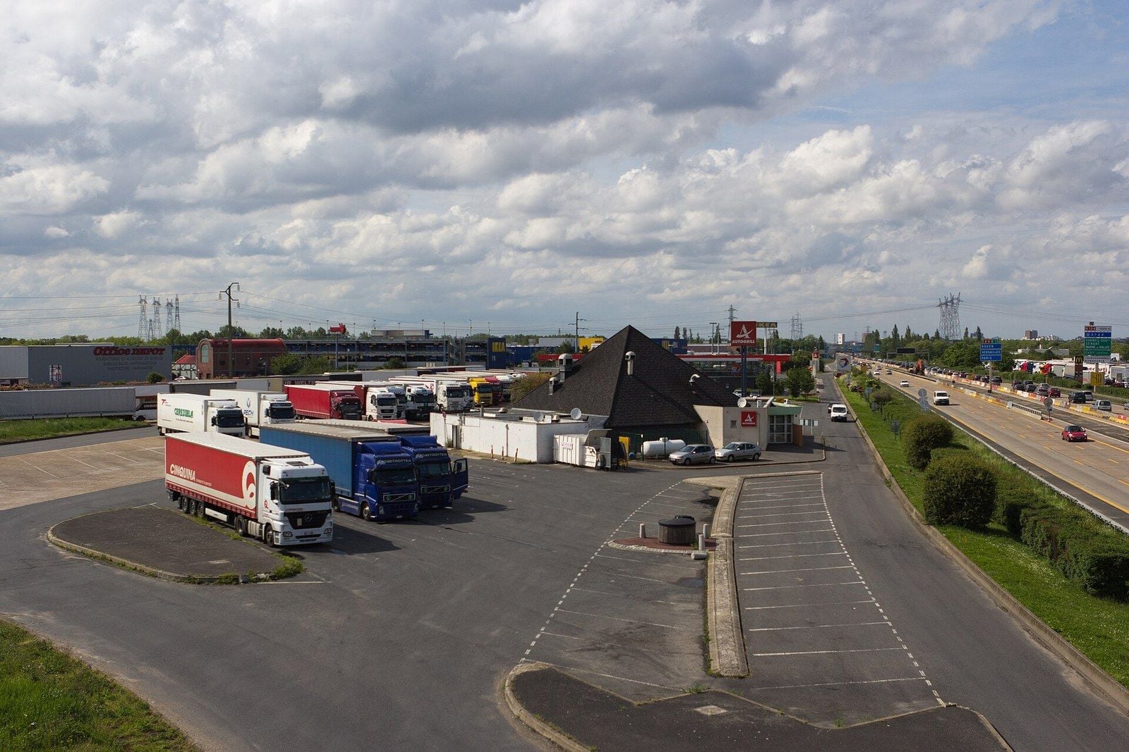 Aire de service de Lisses sur l'A6 à Villabé (Essonne), un dimanche de mai 2012 : des semi-remorques stationnées sur le parking poids lourds près du restaurant de l'aire, et à droite la circulation sur l'autoroute