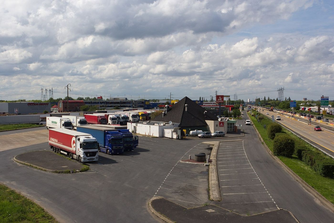Aire de service de Lisses sur l'A6 à Villabé (Essonne), un dimanche de mai 2012 : des semi-remorques stationnées sur le parking poids lourds près du restaurant de l'aire, et à droite la circulation sur l'autoroute