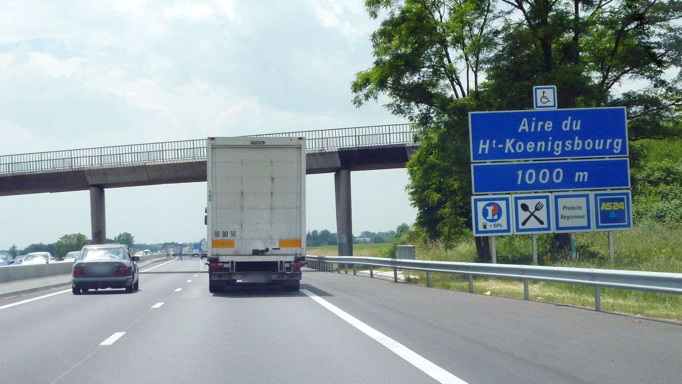 Camion porteur blanc sur l'autoroute A35 en Alsace, avant l'aire du Haut-Koenigsbourg, sous une passerelle ; à gauche une voiture sur la voie de dépassement