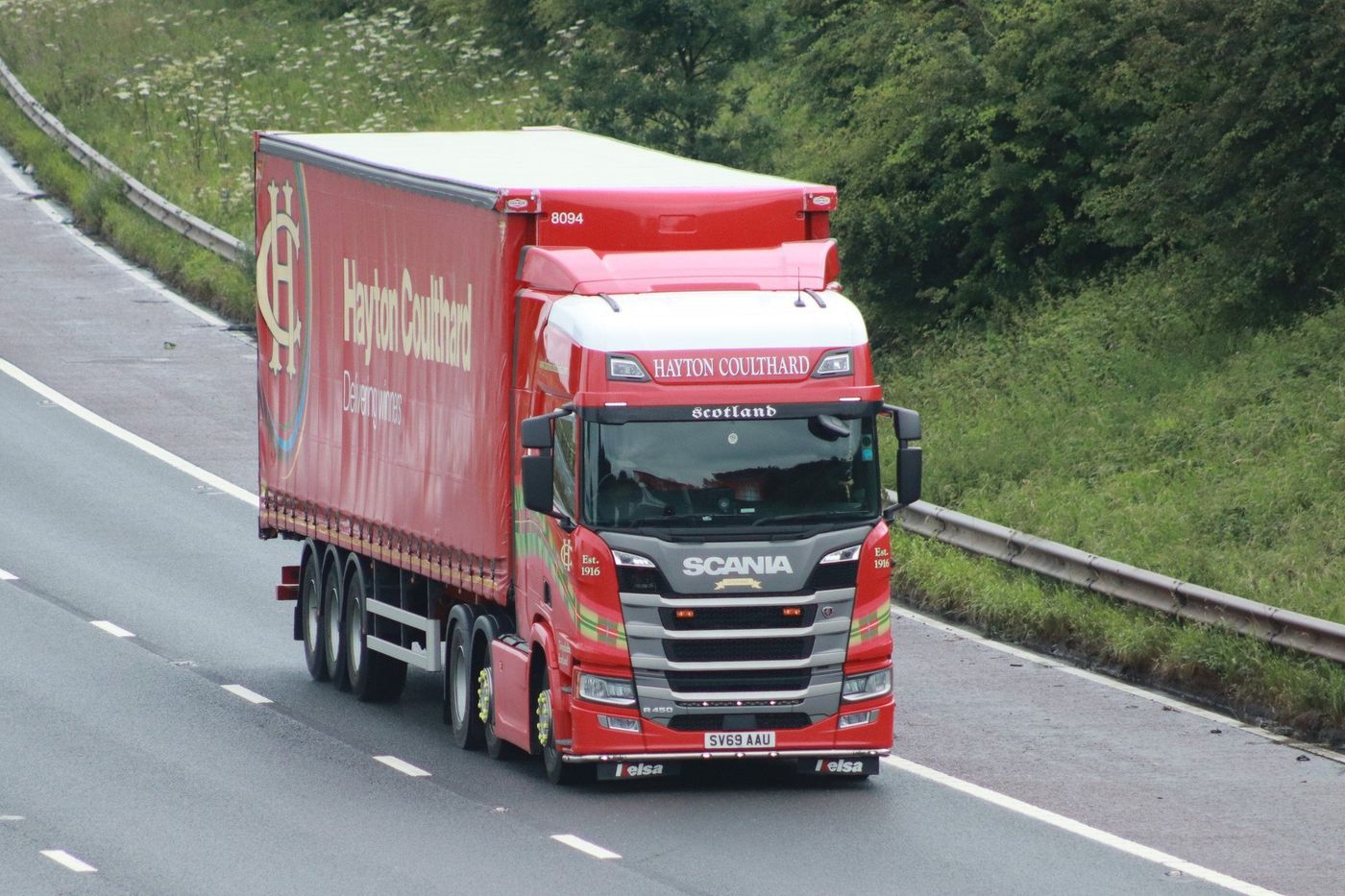 Red tractor unit pulling a curtainsider semi-trailer on a British motorway, with a driver visible in the cab