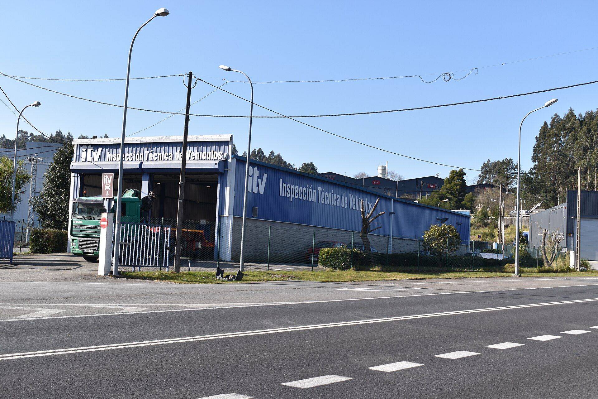 Green truck with a folded loader crane behind the cab, standing in the bay of an ITV vehicle inspection station in Galicia