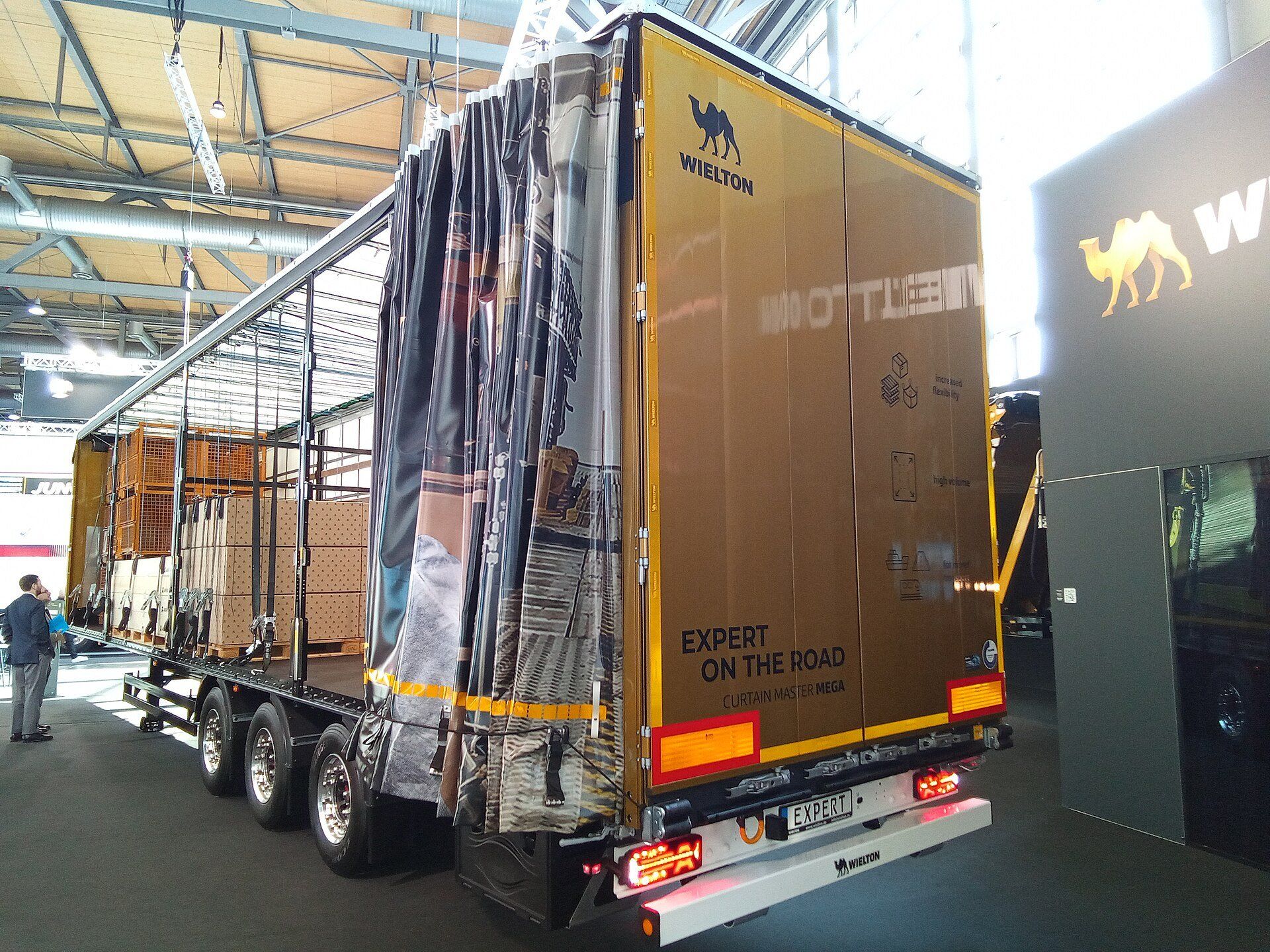 Wielton Curtain Master Mega curtainsider semi-trailer at IAA Transportation 2024 with its curtain drawn back, showing boxed goods on pallets and pallet cages loaded inside