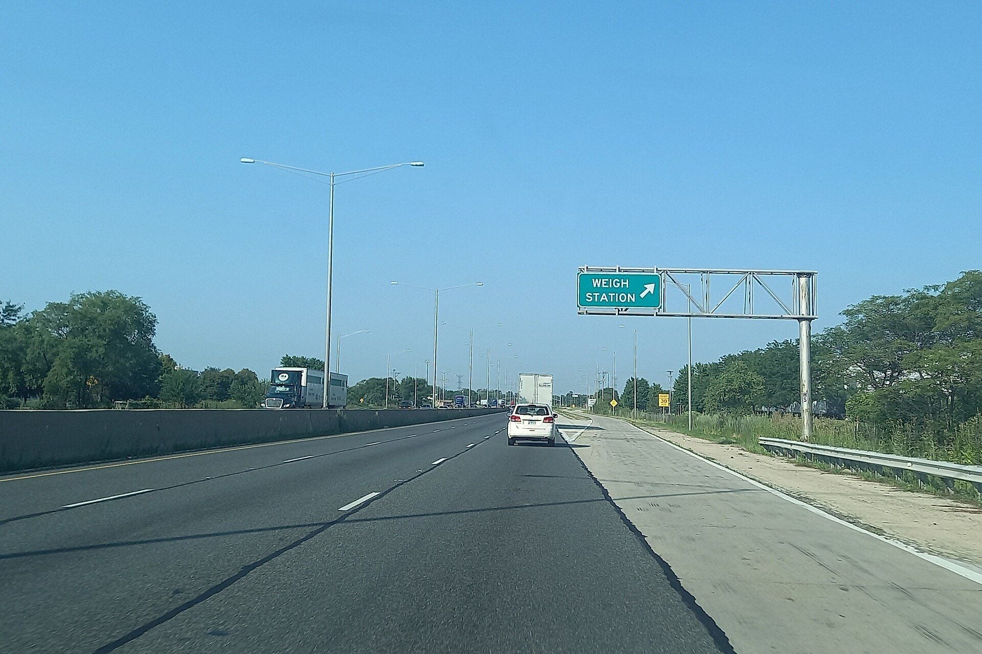 Southbound Interstate 55 in Illinois with an overhead green sign pointing right to the weigh station exit and a semi-truck in the distance
