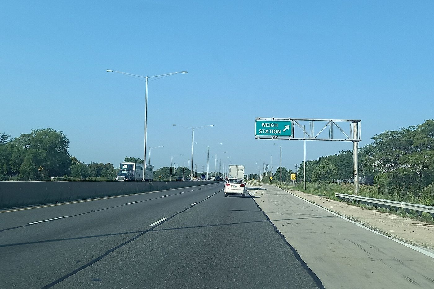 Southbound Interstate 55 in Illinois with an overhead green sign pointing right to the weigh station exit and a semi-truck in the distance