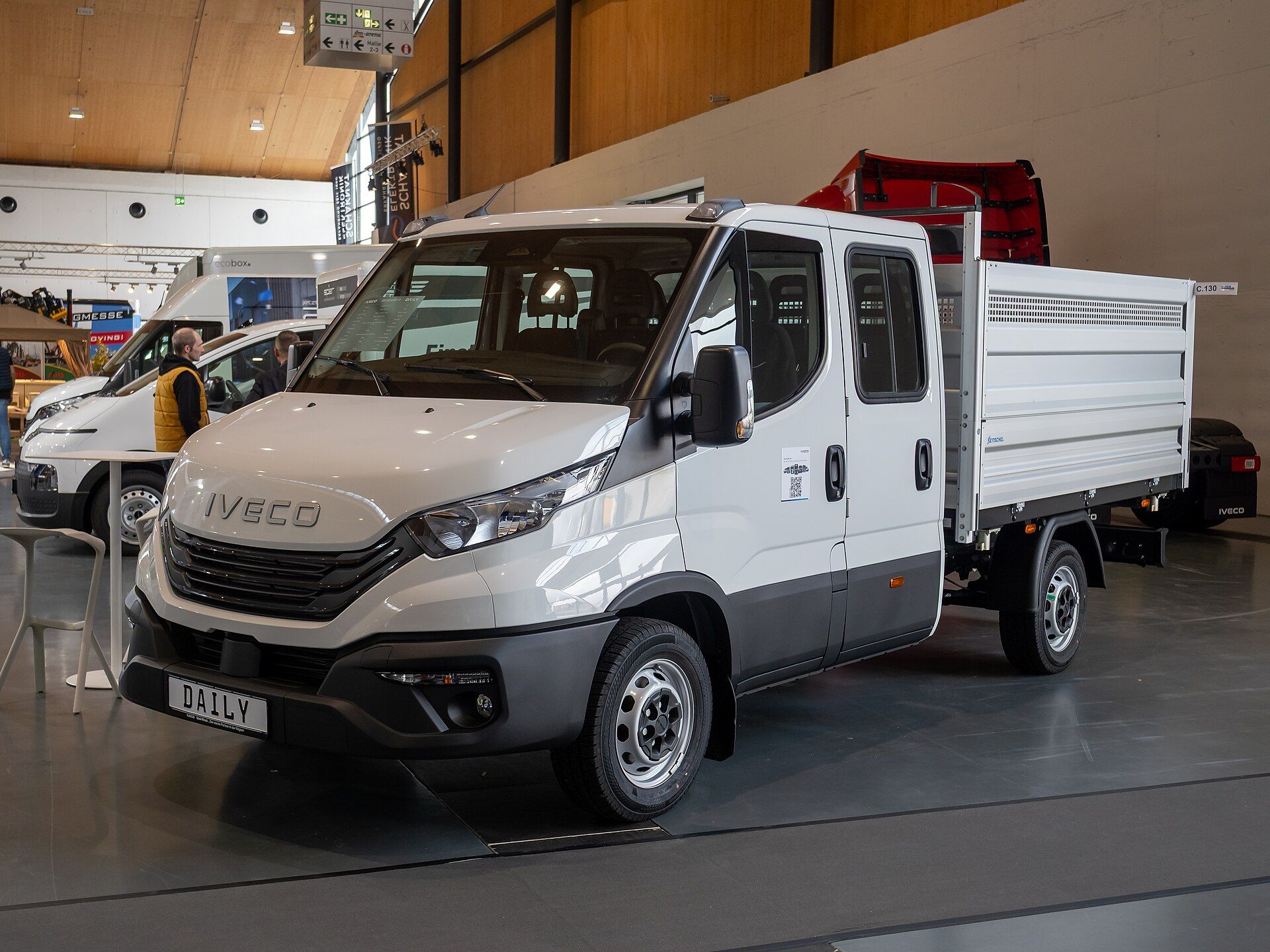 White Iveco Daily crew cab with an aluminium dropside body, single rear wheels and a DAILY plate on the three-piece front bumper, on a stand at the Nufam 2025 trade fair in Rheinstetten