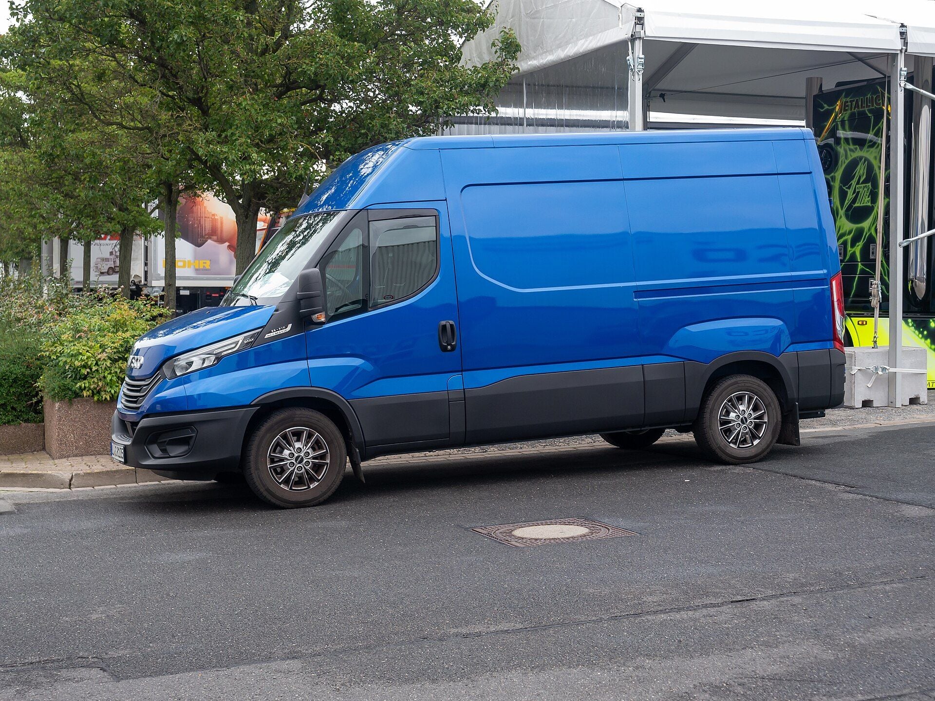 Furgone Iveco Daily blu a ruote posteriori singole, con un badge HI-MATIC dietro il faro, parcheggiato lungo il marciapiede all'IAA Transportation 2024 di Hannover