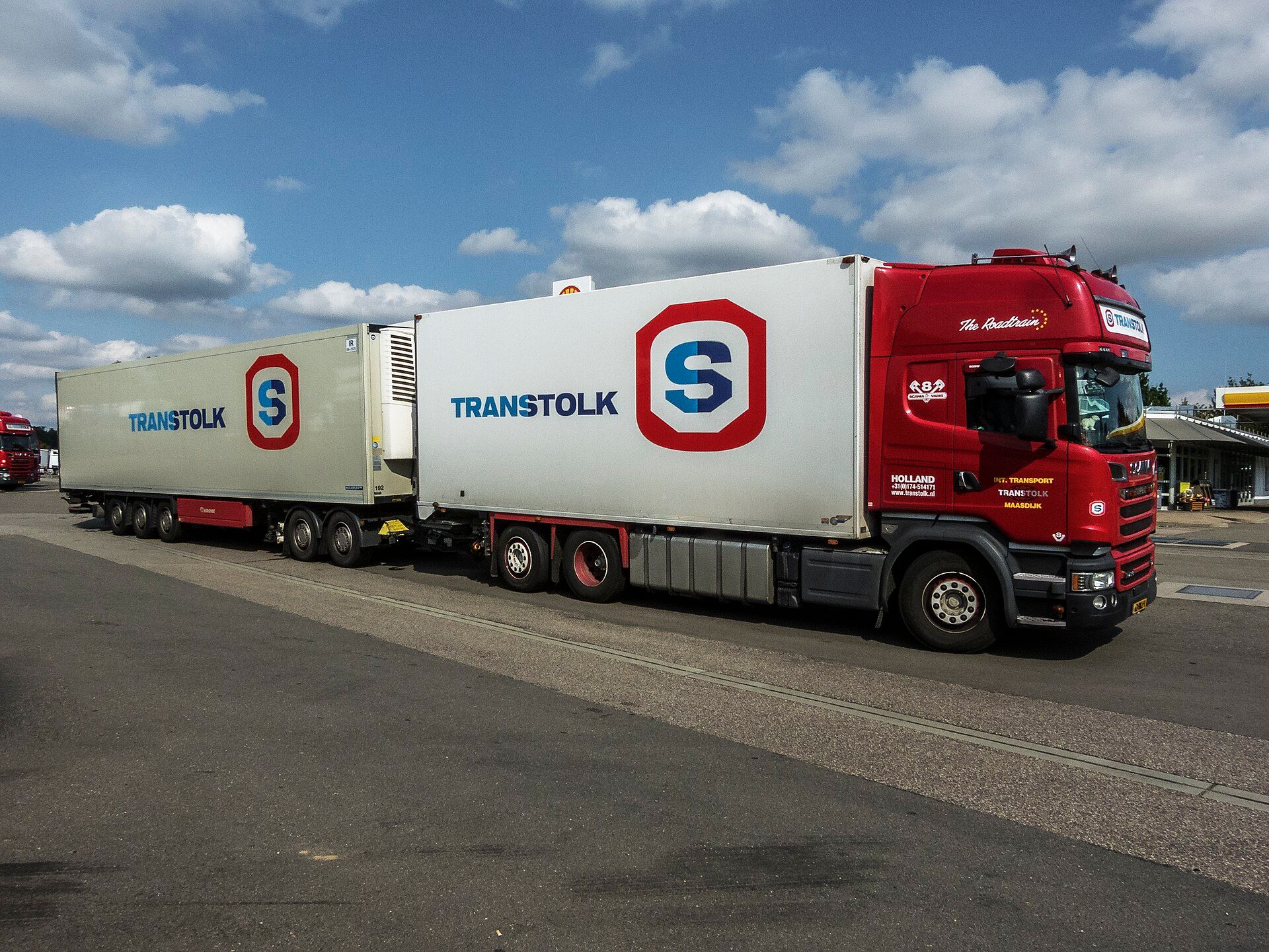 Lange Fahrzeugkombination eines niederländischen Transportunternehmens aus rotem Scania-Motorwagen mit Kofferaufbau, zweiachsigem Dolly und dreiachsigem Kühlauflieger an einer Tankstelle in Schwegenheim