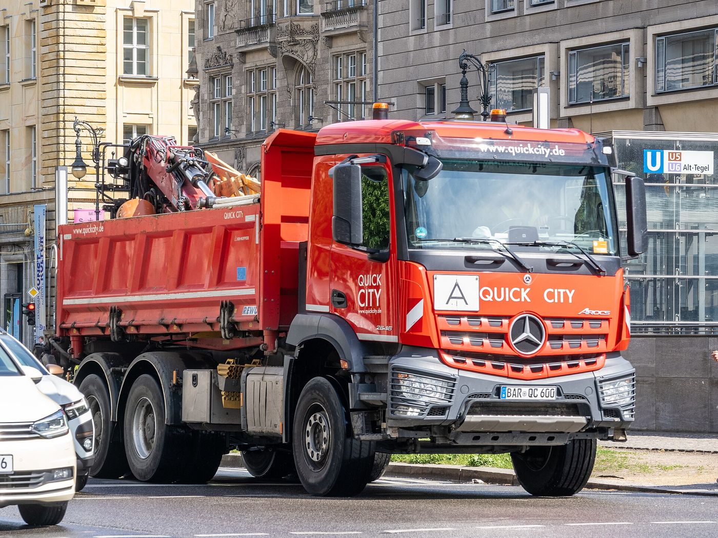 Czerwona trzyosiowa wywrotka Mercedes-Benz Arocs 2646 z żurawiem załadowczym złożonym za kabiną, w ruchu ulicznym w Berlinie