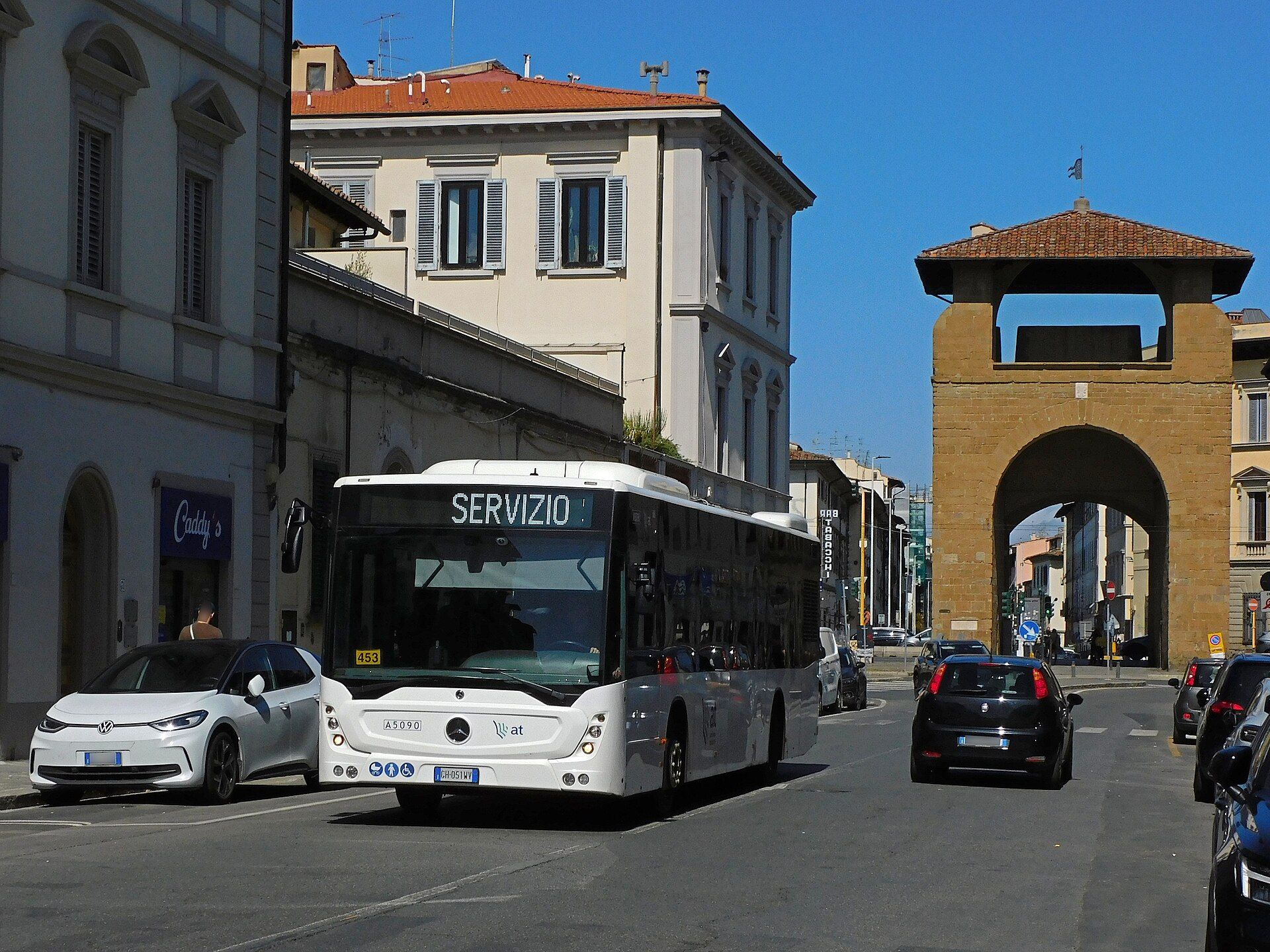 White Mercedes-Benz Conecto two-axle city bus showing SERVIZIO on its destination display, front three-quarter view on via Il Prato in Florence with the Porta al Prato gate behind