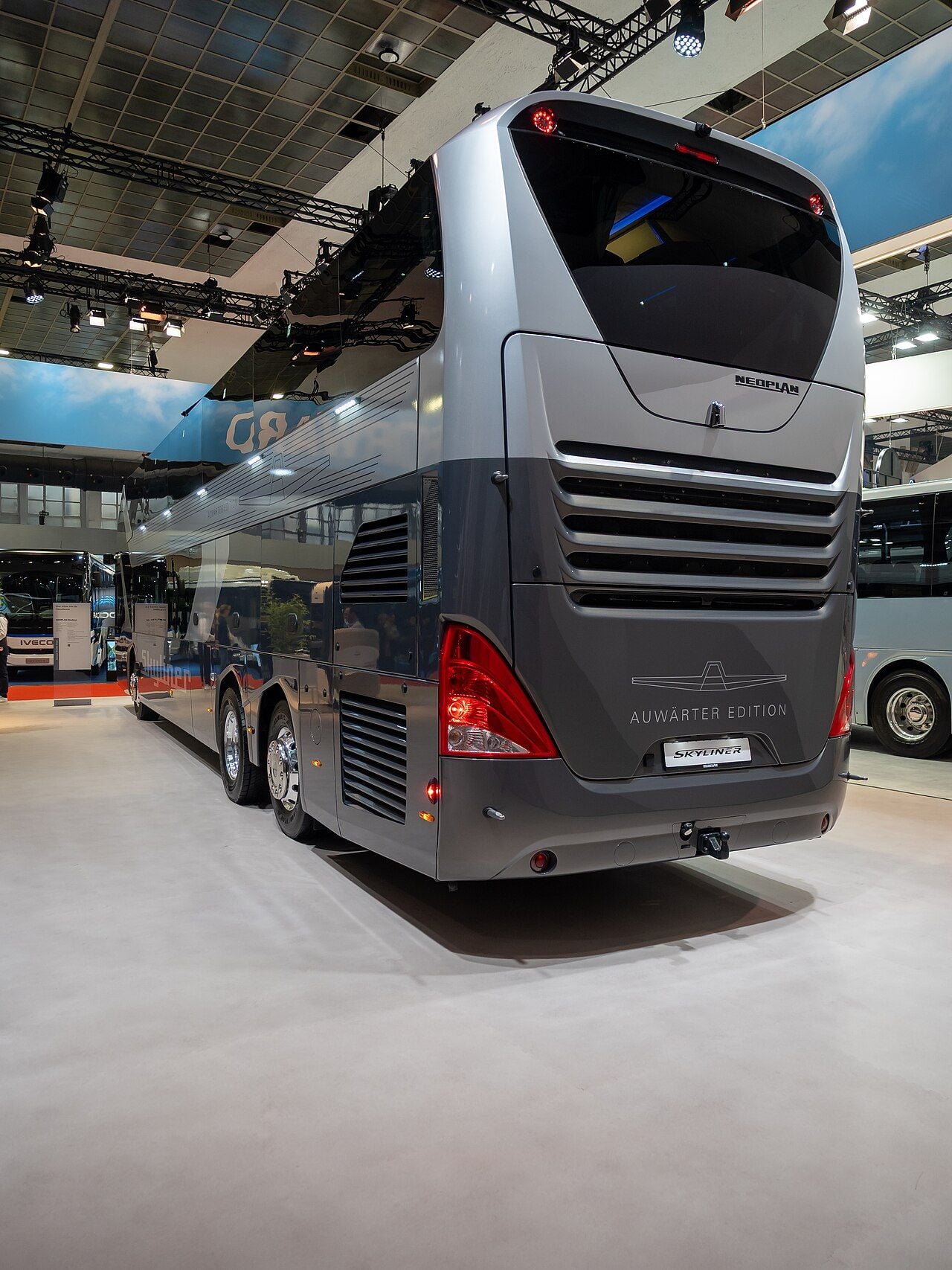 Rear of a grey and silver Neoplan Skyliner with Auwärter Edition lettering and a SKYLINER plate, shown indoors at Busworld Europe 2025 in Brussels