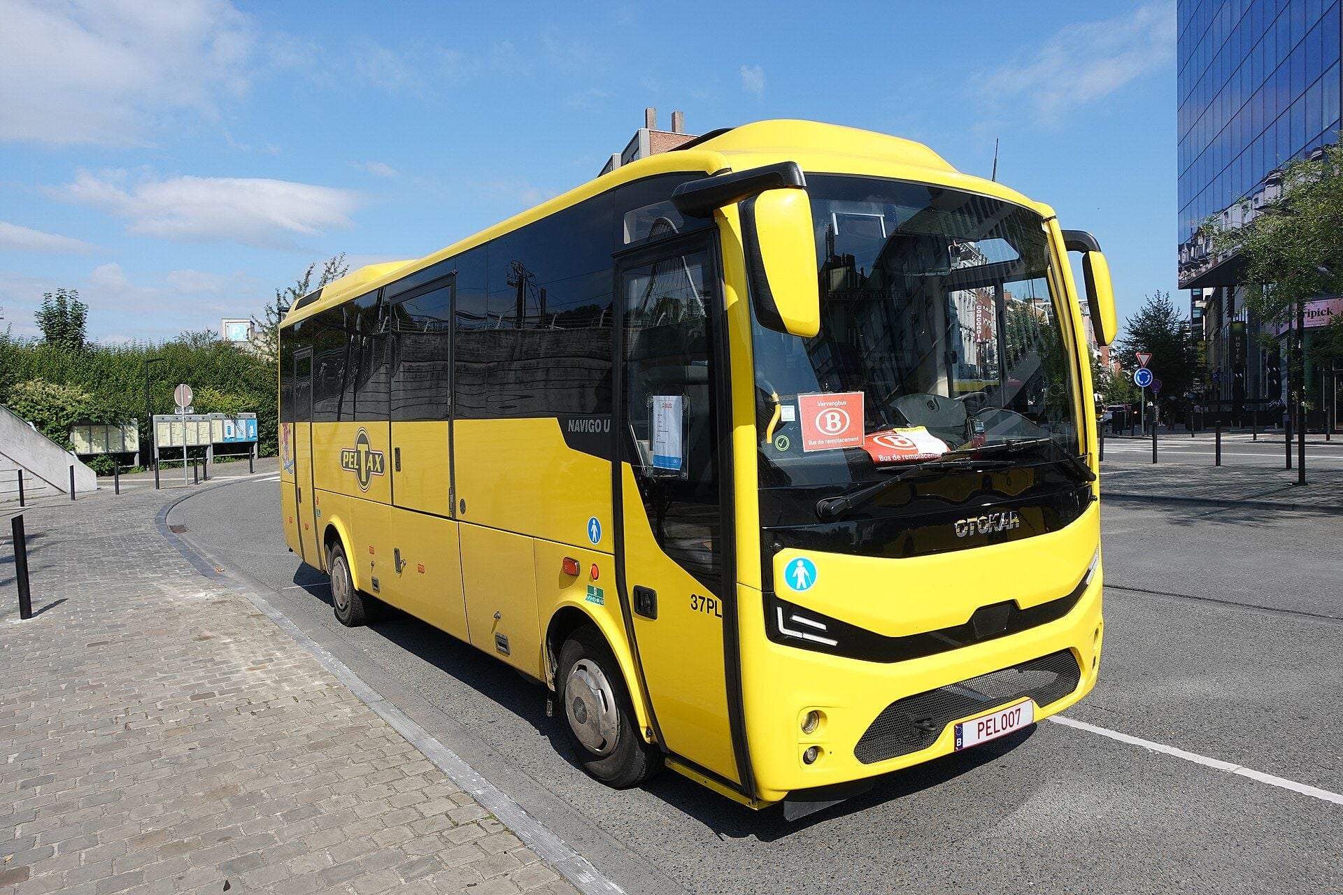 Midibus Otokar Navigo U giallo con una fascia anteriore nera recante il nome OTOKAR e fari spigolosi, in una strada di Liegi, visto dal lato anteriore destro