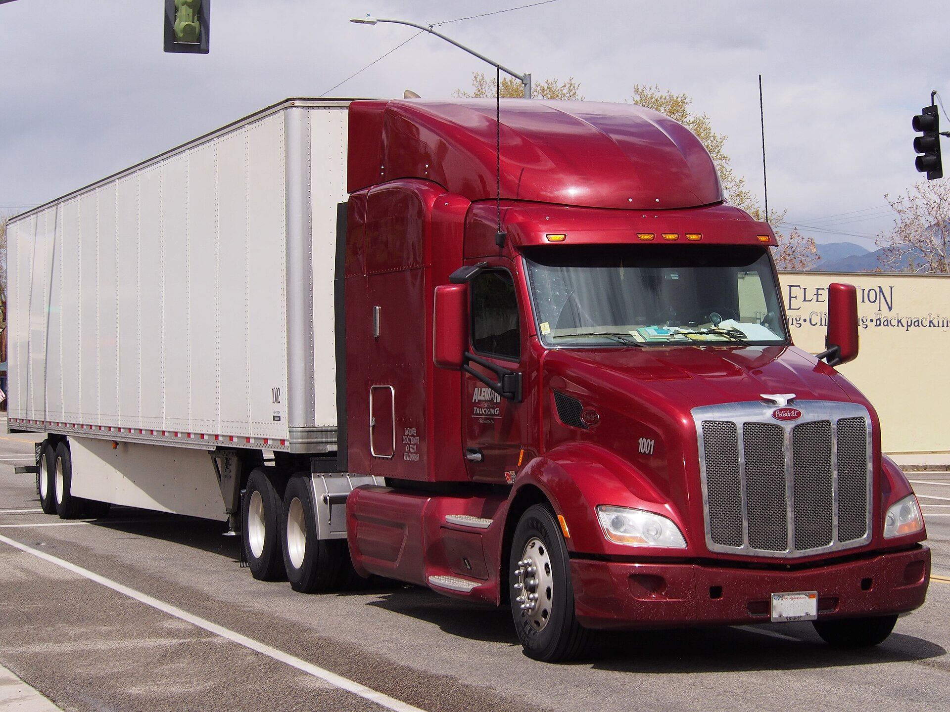 Trattore con cuccetta Peterbilt 579 rosso scuro con carenatura sul tetto, calandra cromata e due assi posteriori, che traina un semirimorchio furgonato bianco lungo la via principale di Lone Pine, in California, fotografato nell'aprile 2018