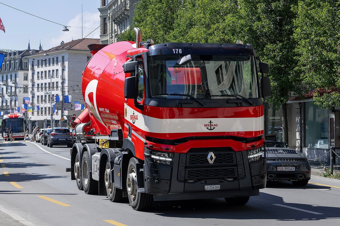 Red and white Renault Trucks C480 four-axle concrete mixer with a honeycomb grille and slim headlamps, driving along a city street under Swiss flags