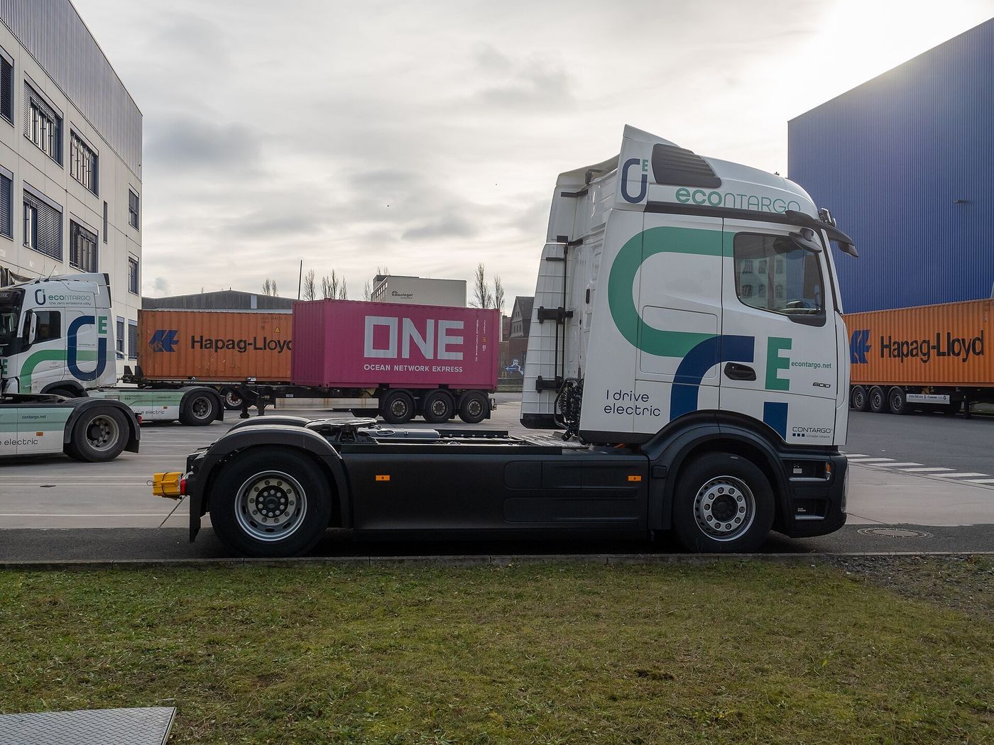 White Mercedes-Benz eActros 600 electric tractor in Contargo livery reading I drive electric at a container terminal in Frankfurt am Main, with shipping containers and a second electric tractor behind it