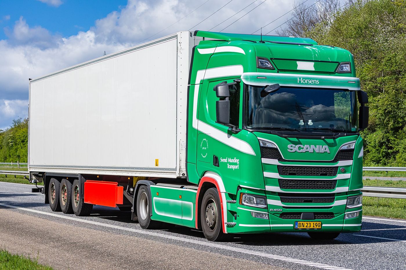 Green Scania R 450 two-axle tractor unit hauling a white three-axle box semi-trailer on a motorway