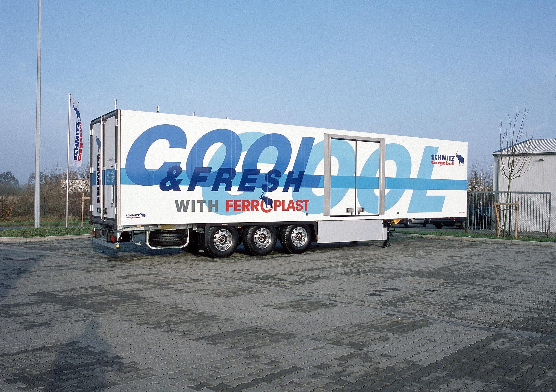 Entkuppelter dreiachsiger Schmitz-Cargobull-Kühlkoffer-Sattelauflieger mit Seitentür, auf den Stützwinden stehend, in der Cool-and-Fresh-FERROPLAST-Vorführlackierung des Herstellers