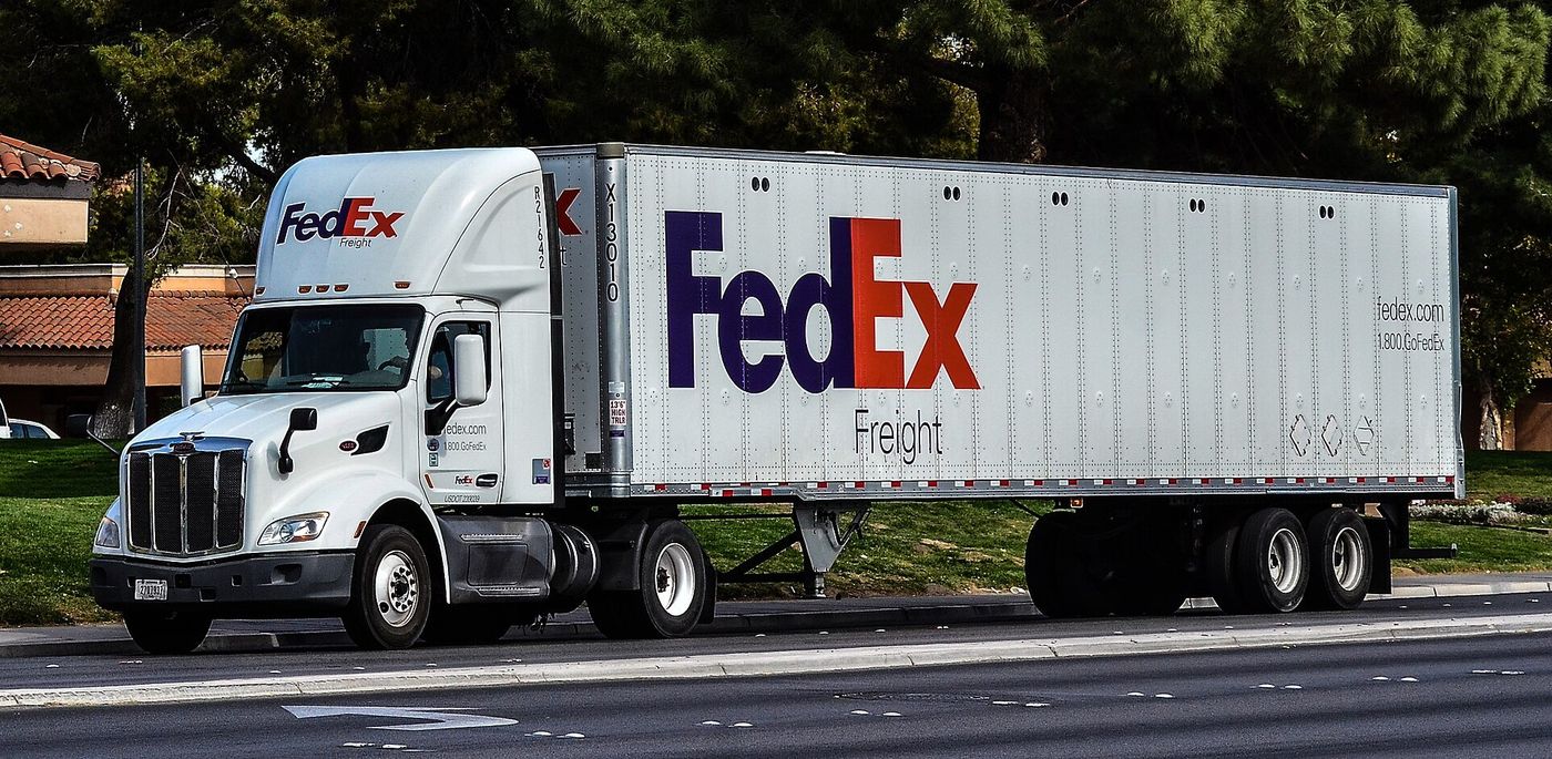 White FedEx Freight Peterbilt day-cab tractor pulling a long white FedEx Freight semitrailer, seen side-on from across a road