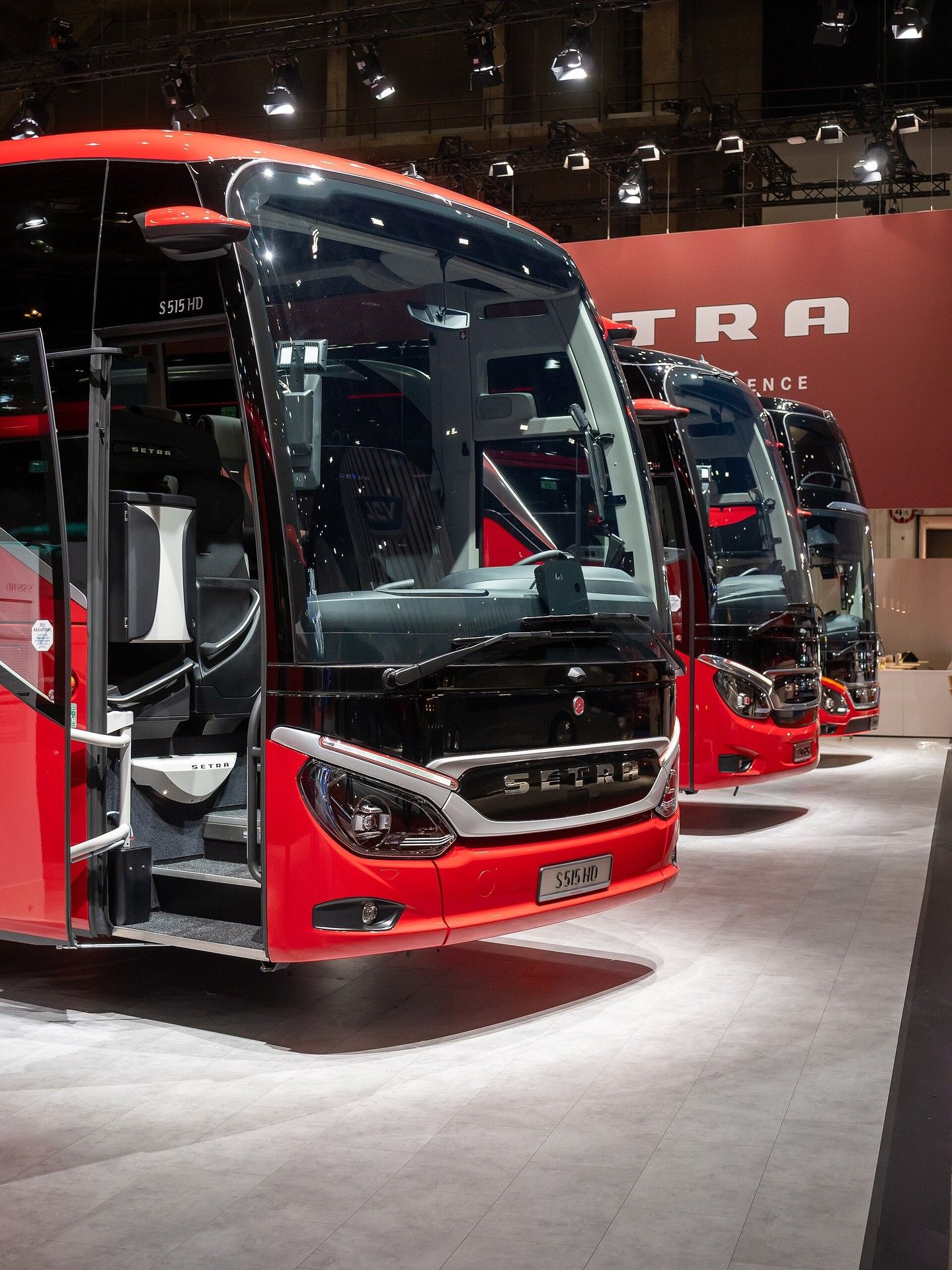 Red Setra ComfortClass S 515 HD with its front door open, first in a row of Setra coaches on the Setra stand at Busworld Europe 2025 in Brussels, seen from the front right