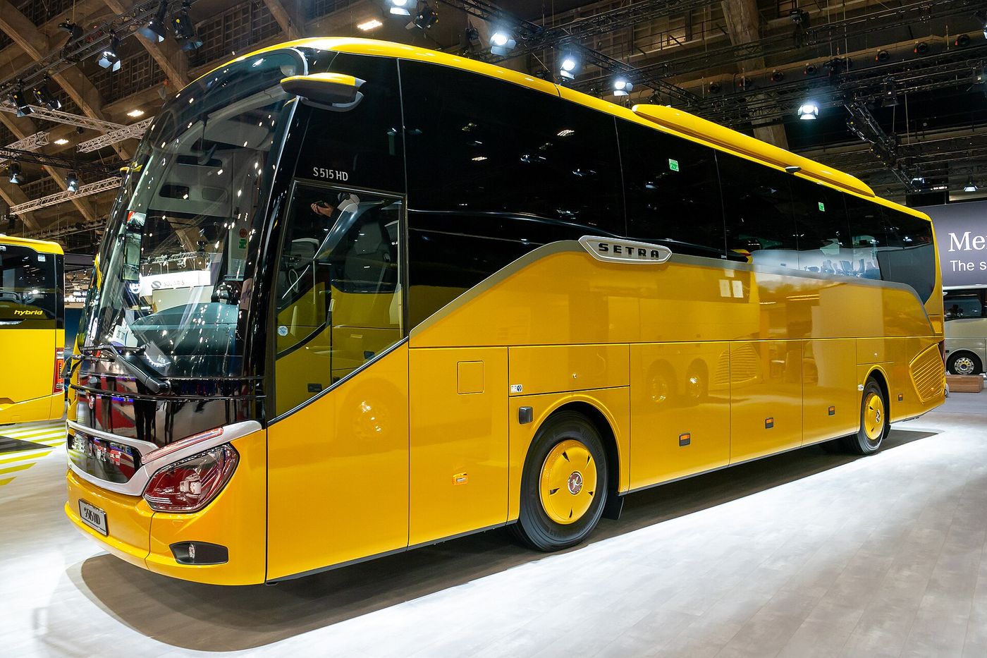 Yellow Setra ComfortClass S 515 HD two-axle high-deck touring coach with a black front panel and silver trim on an exhibition stand at Busworld Europe 2023 in Brussels, seen from the front right