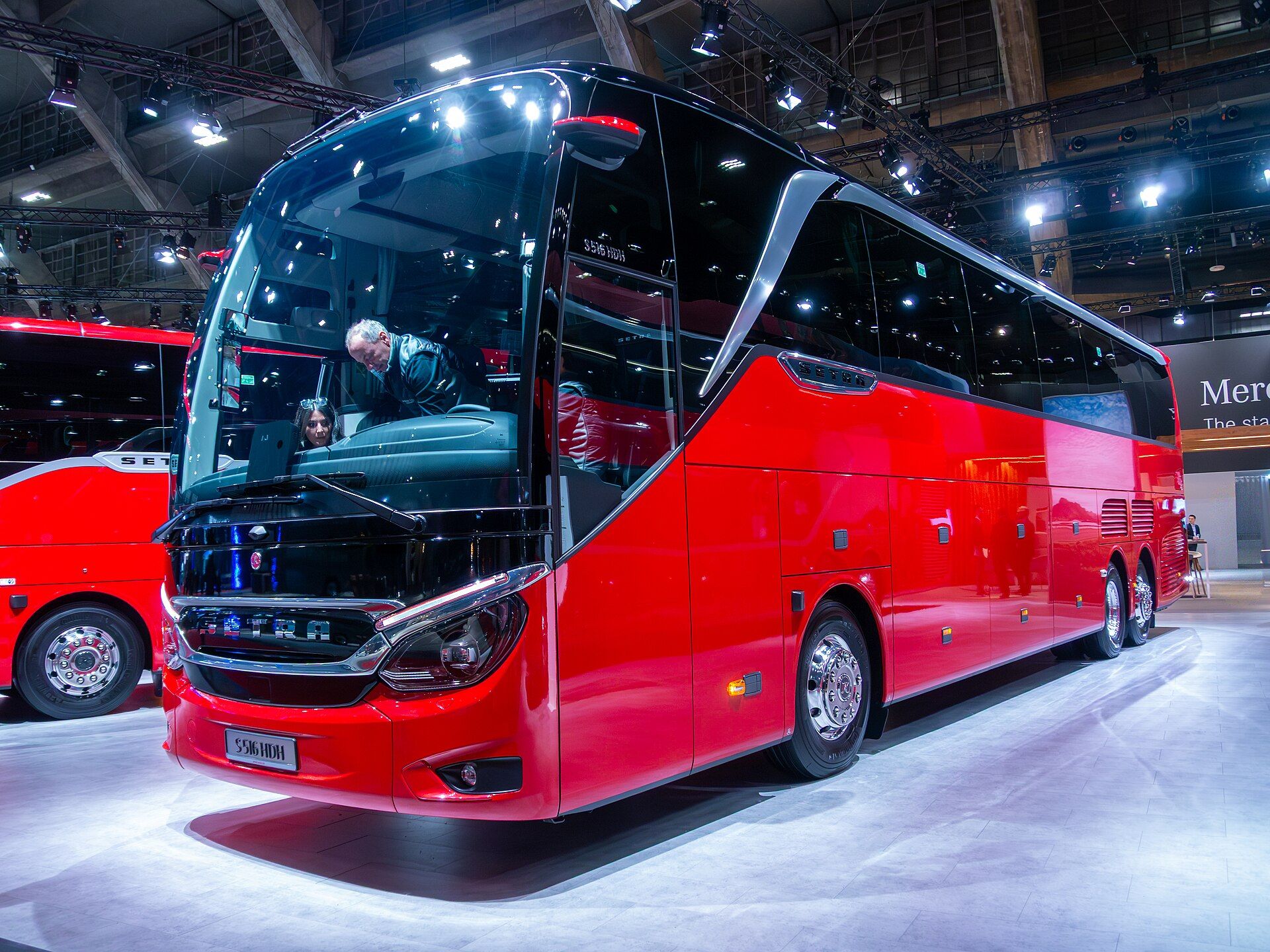 Red Setra TopClass S 516 HDH seen from the front left on an exhibition stand at Busworld Europe 2025, showing the driver's side and its three axles