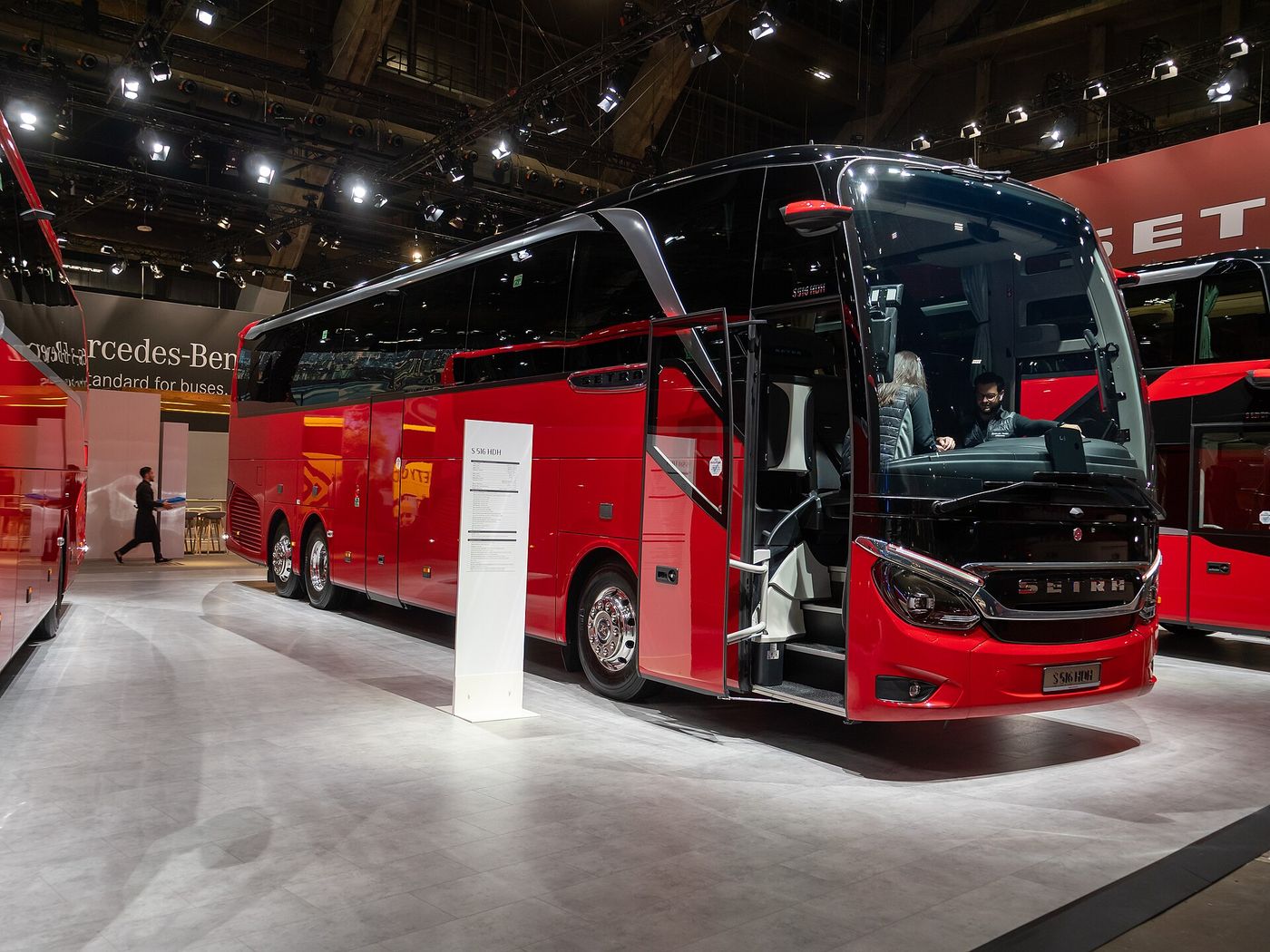 Red Setra TopClass S 516 HDH three-axle high-deck touring coach with its front door open on the Setra stand at Busworld Europe 2025 in Brussels, seen from the front right