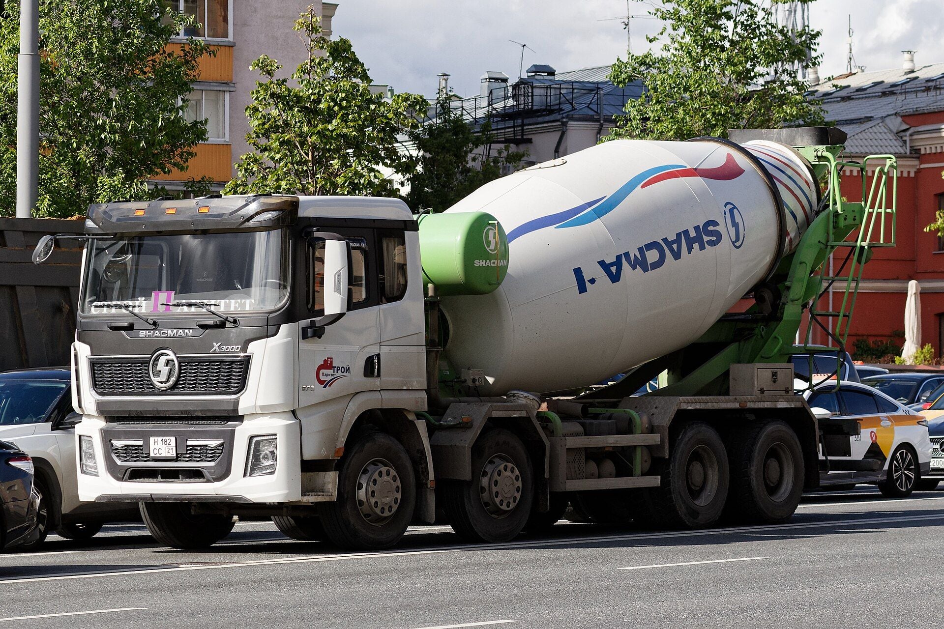 White SHACMAN X3000 four-axle truck mixer with a flat-roof cab, a white drum with SHACMAN lettering and a green mixer frame, turning on a Moscow street among cars