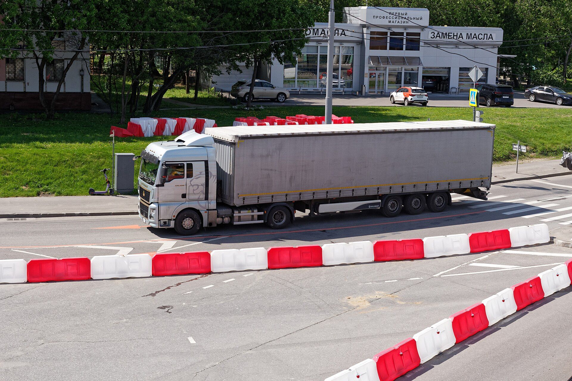 Silver SITRAK C7H 480 two-axle tractor unit with a grey curtainside semi-trailer, seen from above on a Moscow street lined with red and white water-filled barriers in May 2026