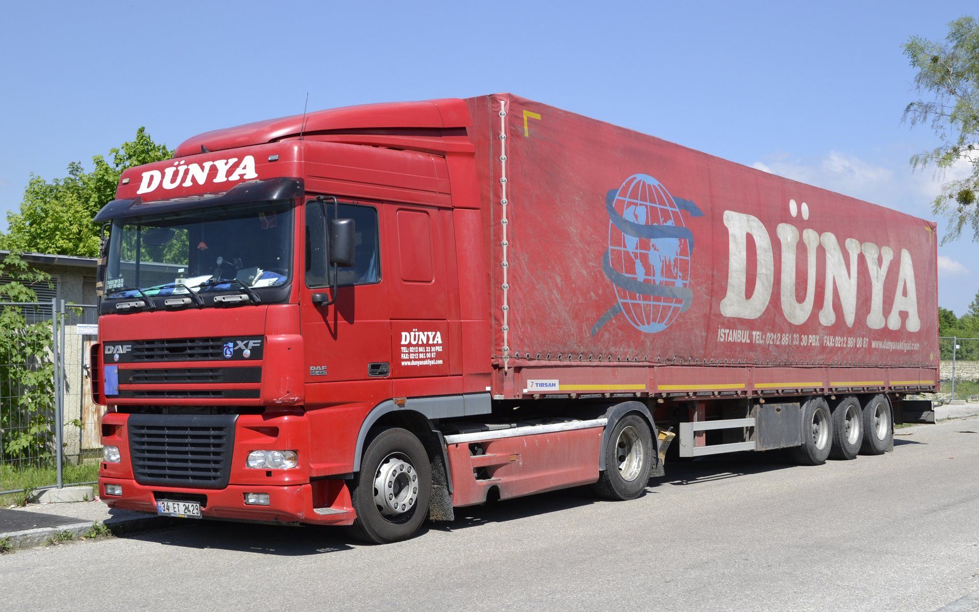 Münih'te çekilmiş fotoğraf: Türk plakalı (34) kırmızı bir DAF XF çekici ve tenteli üç dingilli yarı römork, yol kenarında park halinde