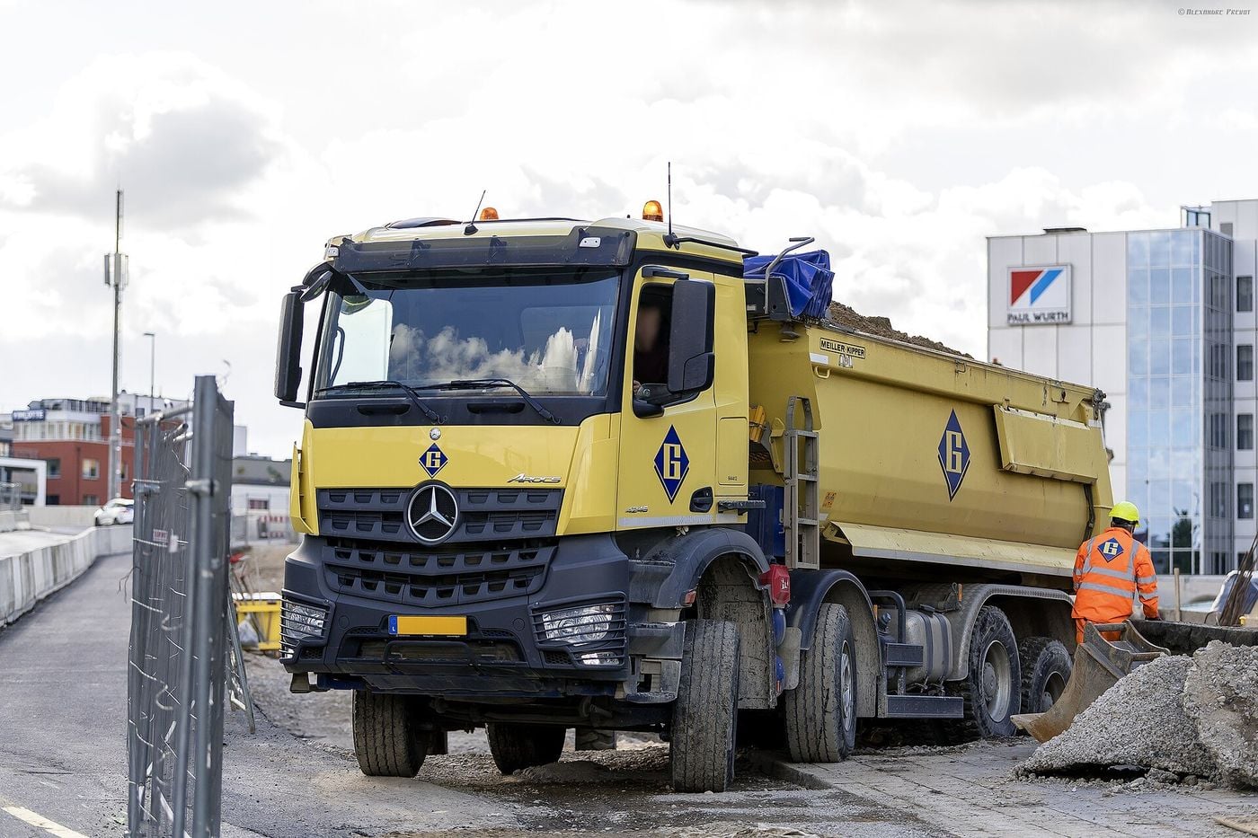 Lüksemburg'da bir şantiyede, önde iki ve arkada iki dingili olan sarı damperli Mercedes-Benz Arocs 4246 kamyon