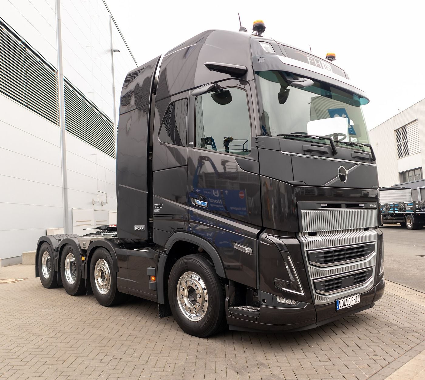 Black Volvo FH16 780 four-axle 8x4 heavy-haulage tractor unit without a trailer, parked on paving beside an exhibition hall at IAA Transportation 2024