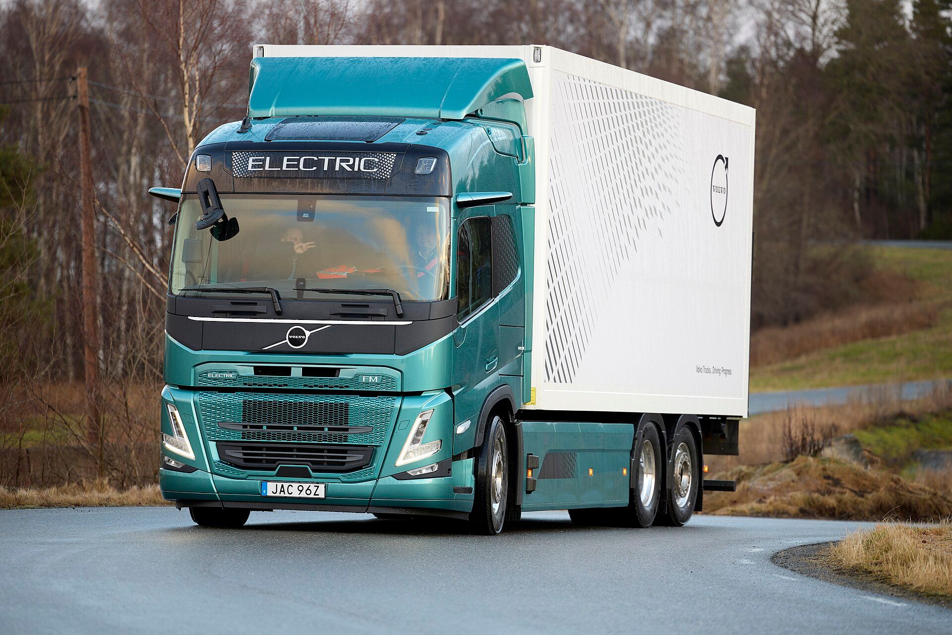 Green Volvo FM Electric three-axle rigid with a white box body and an ELECTRIC sign above the windscreen, on a country road