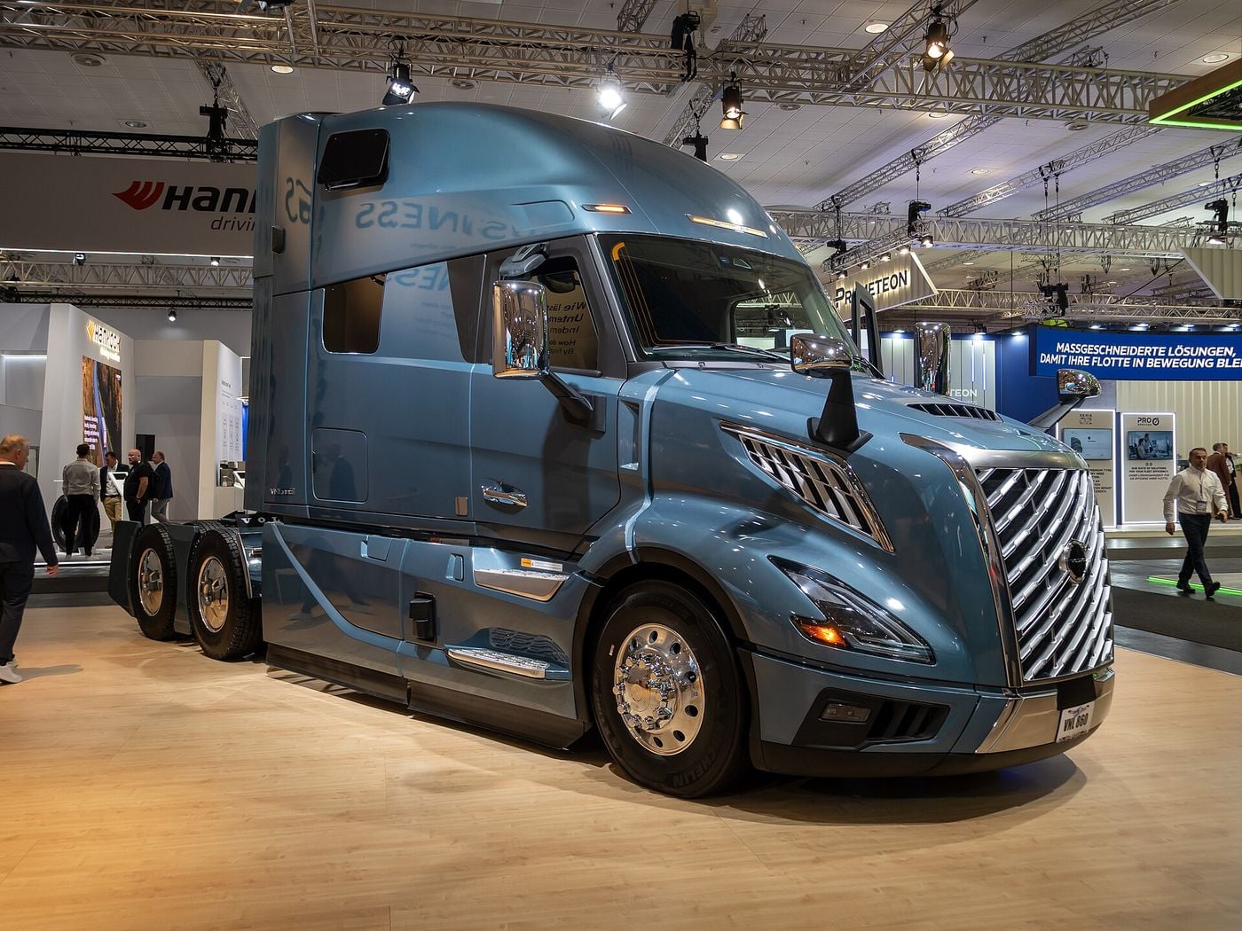 Blue-grey Volvo VNL 860 high-roof sleeper tractor with two rear axles seen from the front right, showing the curved windshield, the angled chrome grille and the double-V headlamps, at IAA Transportation 2026 in Hanover